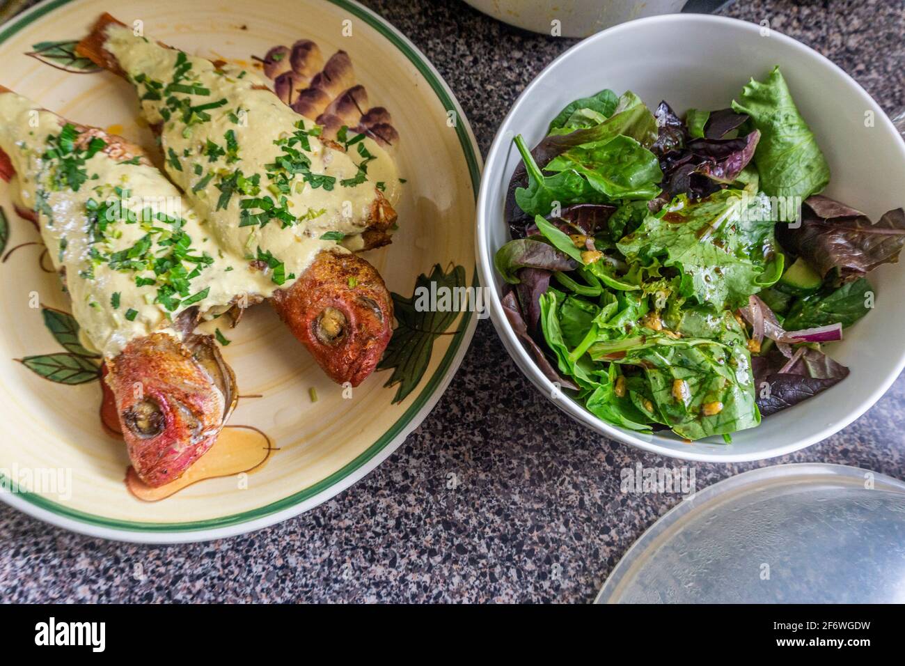 Gebratener Fisch mit Sauce auf einem Teller und einer Schüssel Salat an der Seite Stockfoto