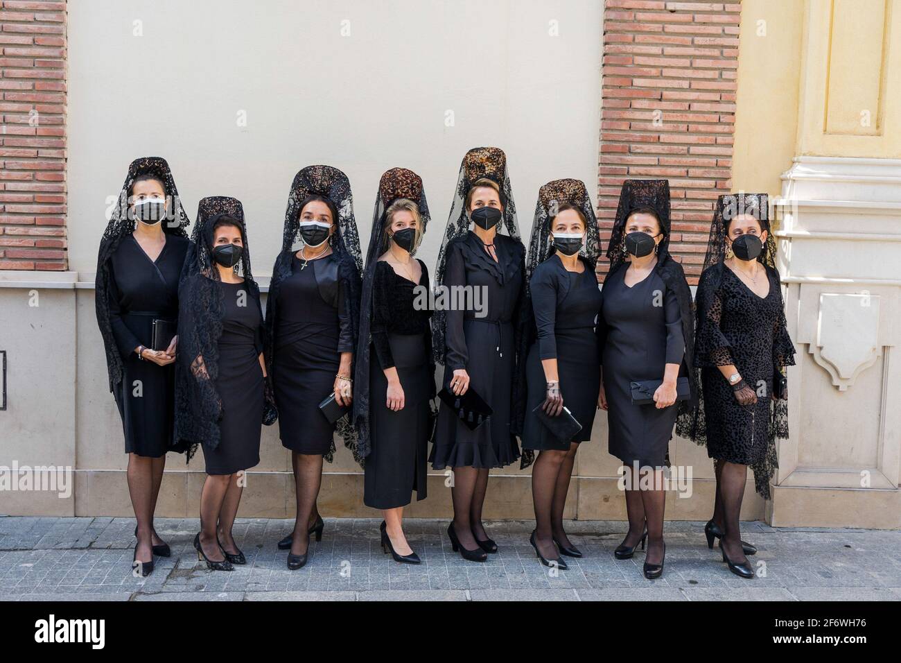 Malaga, Spanien. März 2021. Frauen in Mantilla-Kleidern und Gesichtsmasken  posieren für ein Foto während des Karfreitags. Traditionell tragen Frauen  in Spanien Mantilla-Kleider als Trauerkleidung, während sie die Jungfrau  während der Prozessionen der