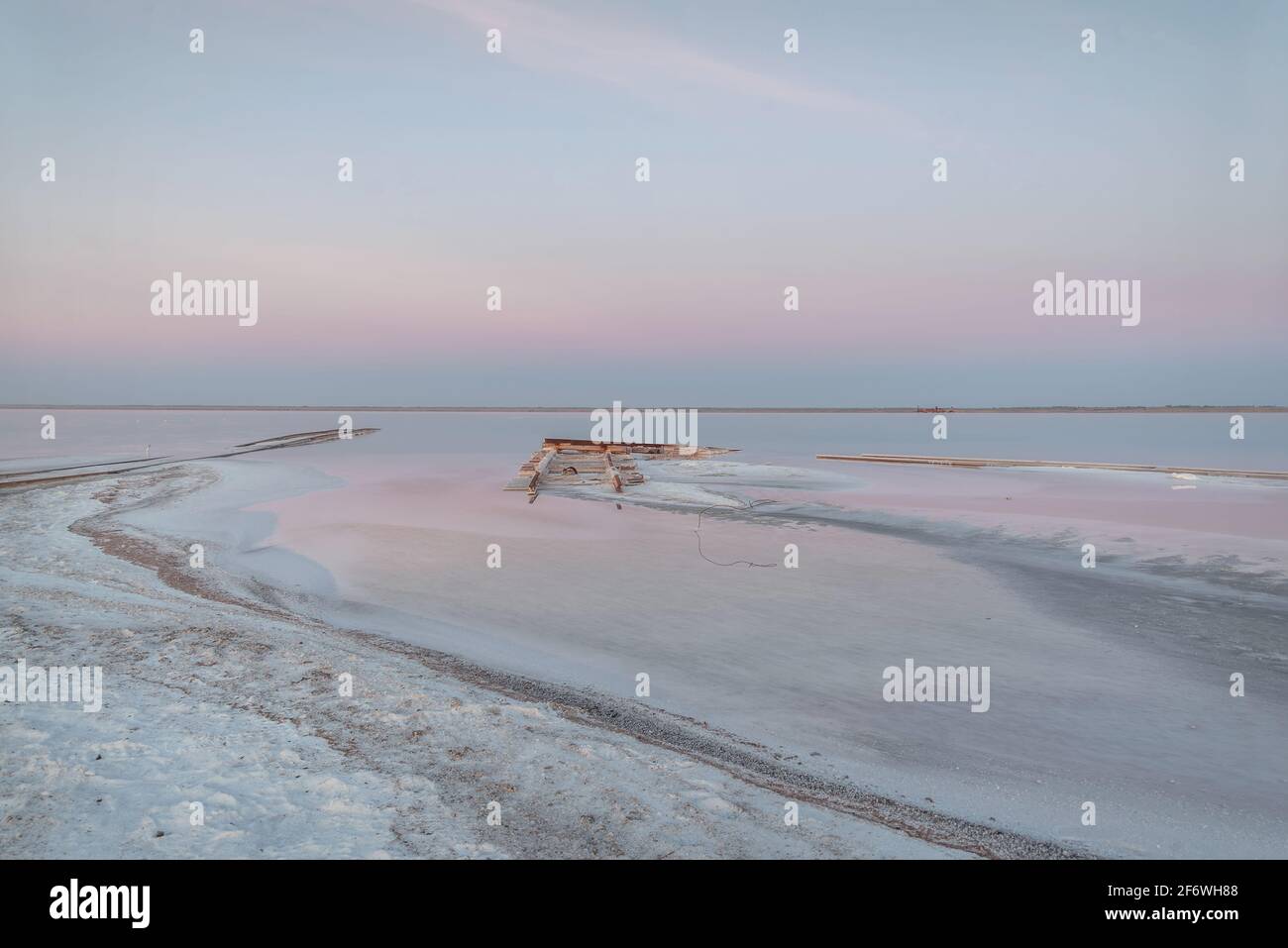 Erstaunlicher zartrosa Sonnenaufgang über einem Salzsee, Schienen ins Wasser und Salz am Ufer im Vordergrund. Lake Bursol, Altai-Territorium, Russ Stockfoto