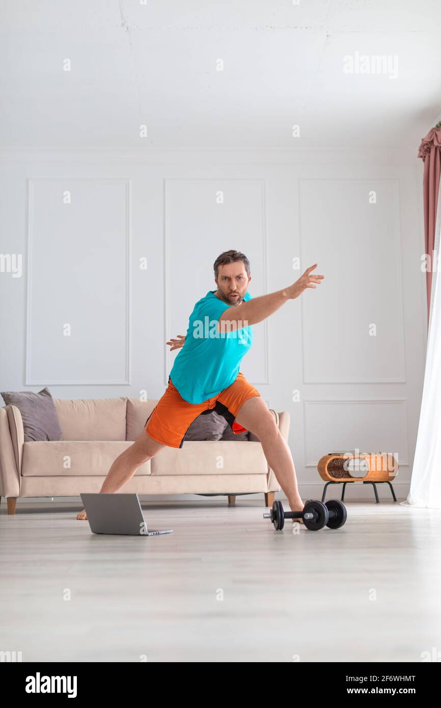 Mann mittleren Alters beim Online-Aerobic-Training. Home Workout-Konzept. Schweres Training zu Hause vor dem Laptop-Monitor. Stockfoto