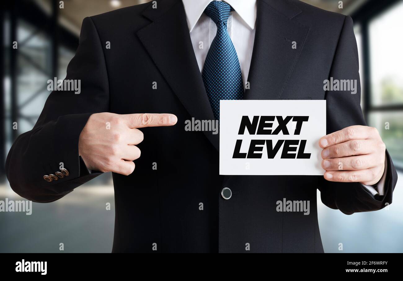Geschäftsmann zeigt eine Karte mit der Botschaft Next Level. Fortschritt, Wachstum, Entwicklung oder Verbesserung des Karrierekonzepts. Stockfoto