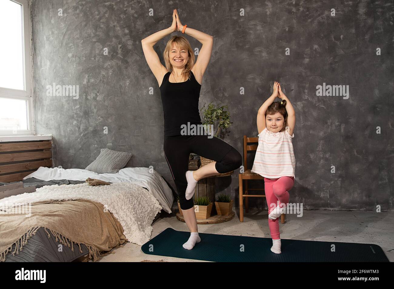 Junge Frau und Tochter machen Yoga-Übungen und Stretching zu Hause. Gesundheit, Sport, Freizeitkonzept. Mutter und kleines Mädchen üben zusammen Stockfoto