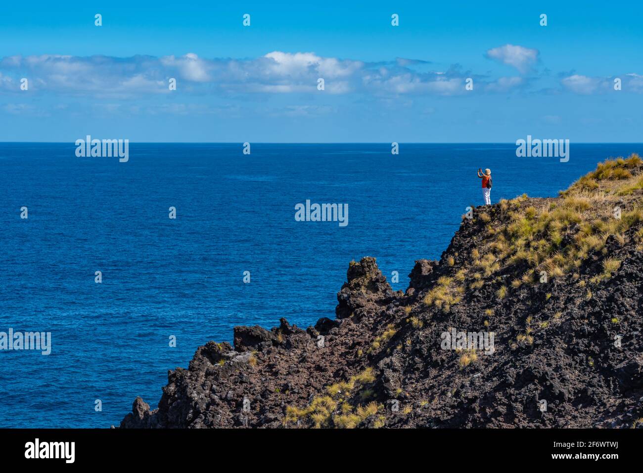 Frau, die auf einem Felsen steht und den Blick auf das Meer bei Sao Miguel, Azoren, den wunderschönen blauen Himmel genießt Stockfoto