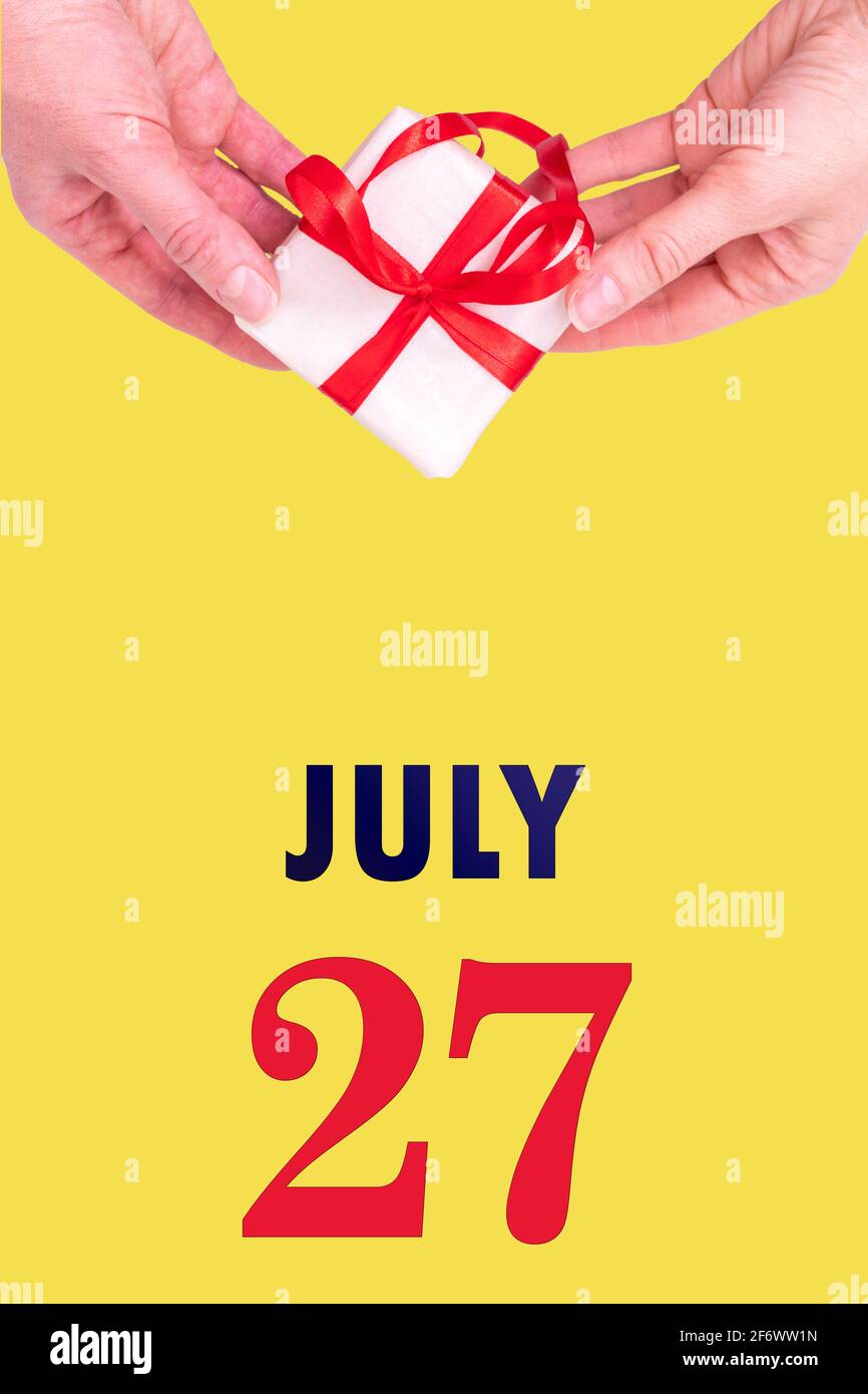 Juli. Festlicher vertikaler Kalender mit Händen Halten weiße Geschenkschachtel mit rotem Band und Kalenderdatum auf leuchtend gelbem Hintergrund.Sommer mont Stockfoto