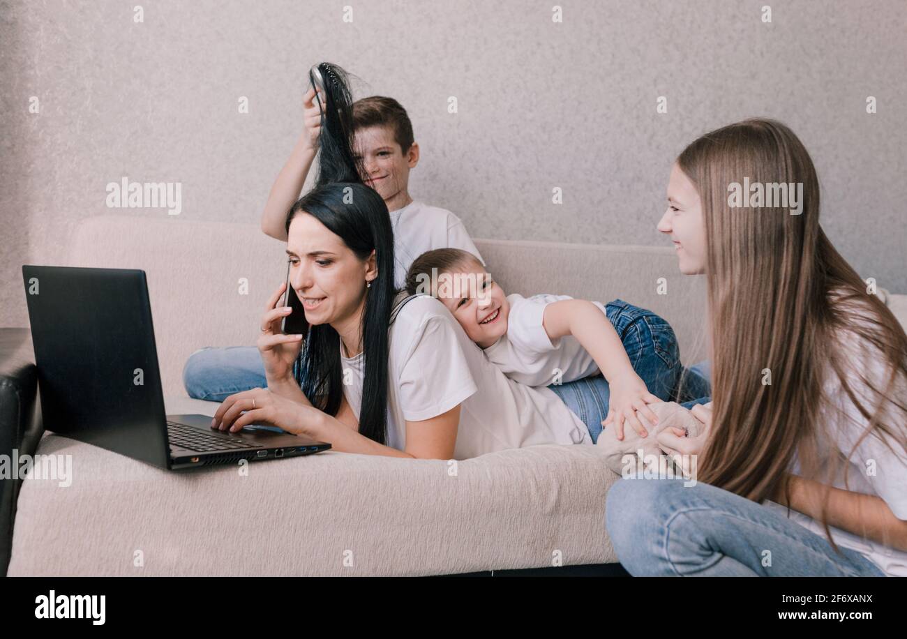 Aktive Kinder frönen, stören und ablenken ihre Mutter, während sie zu Hause auf einem Laptop arbeiten Stockfoto