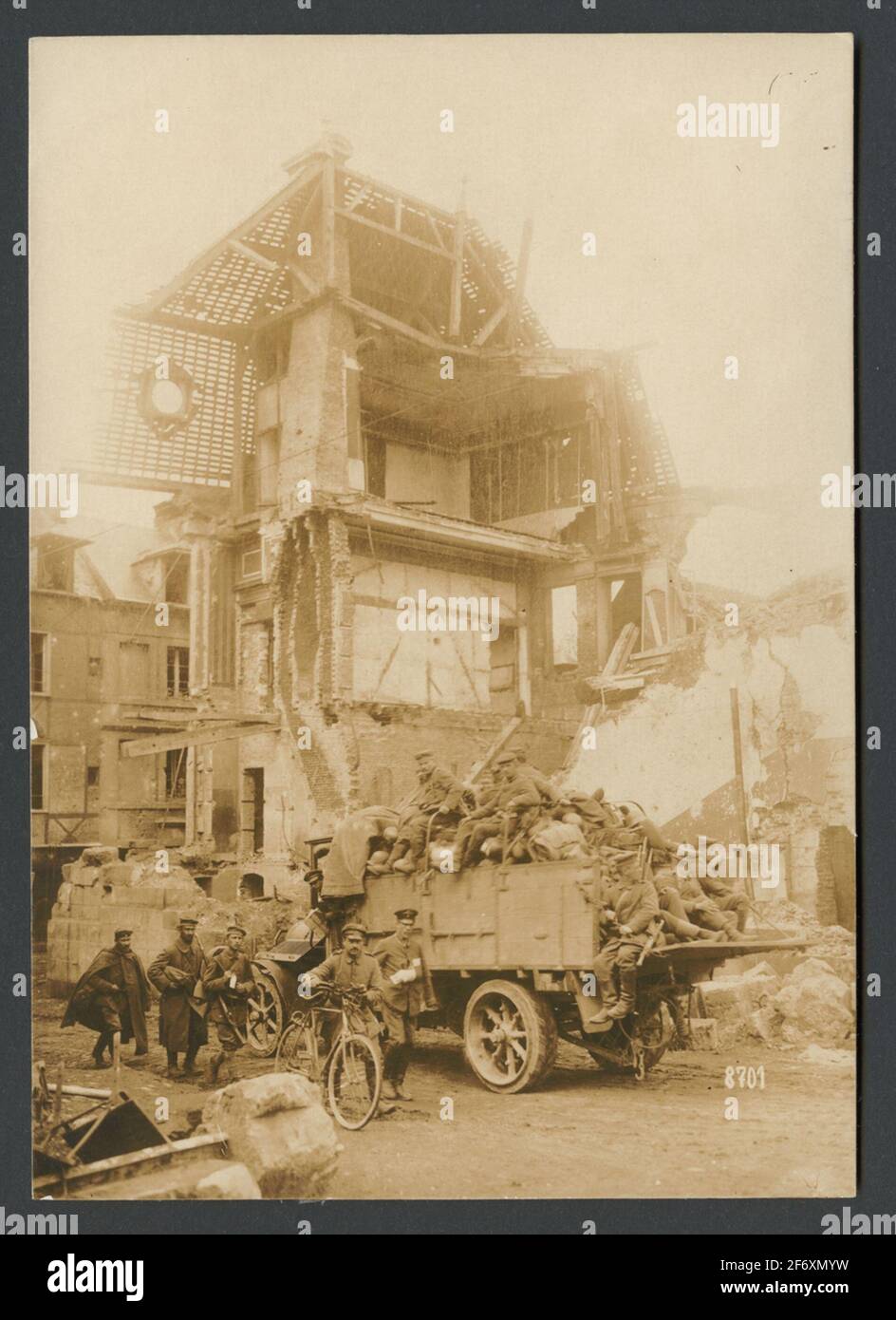 Das Bild zeigt Soldaten, die sich auf einer Straße vor einer Ruine in einer geklebten Stadt bewegen.im Vordergrund geht eine Gruppe zu Fuß.EINE Person führt ein Fahrrad, Neben ihm geht ein verwundete einen verputzten Arm, hinter dem sie einen Lastwagen fahren, der zu Kriegsmaterial transportiert wird und Soldaten auf der Flocke sitzen. Das Bild zeigt Soldaten, die sich auf einer Straße vor einer Ruine in einer zerbrochenen Stadt bewegen.im Vordergrund geht eine Gruppe zu Fuß.EINE Person führt ein Fahrrad, Neben ihm geht ein verwundete einen verputzten Arm, hinter dem sie einen Lastwagen fahren, der zu Kriegsmaterial transportiert wird und Soldaten auf der Flocke sitzen. Stockfoto