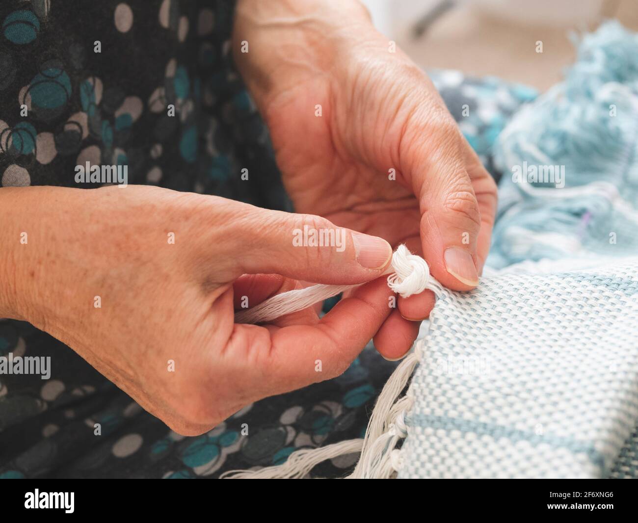 Die Frau bindet Knoten, um einen Rand auf einem gewebten Stoff zu schaffen. Fertigstellung einer Webart. Konzept des Handwerks, Handarbeit Stockfoto
