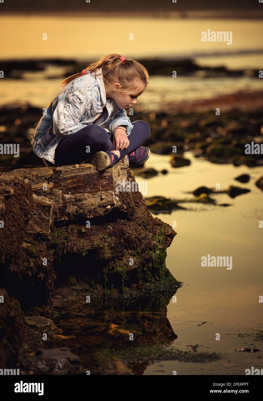 Mädchen, das auf einem Küstenfelsen sitzt und in den Ozean blickt, Irland Stockfoto