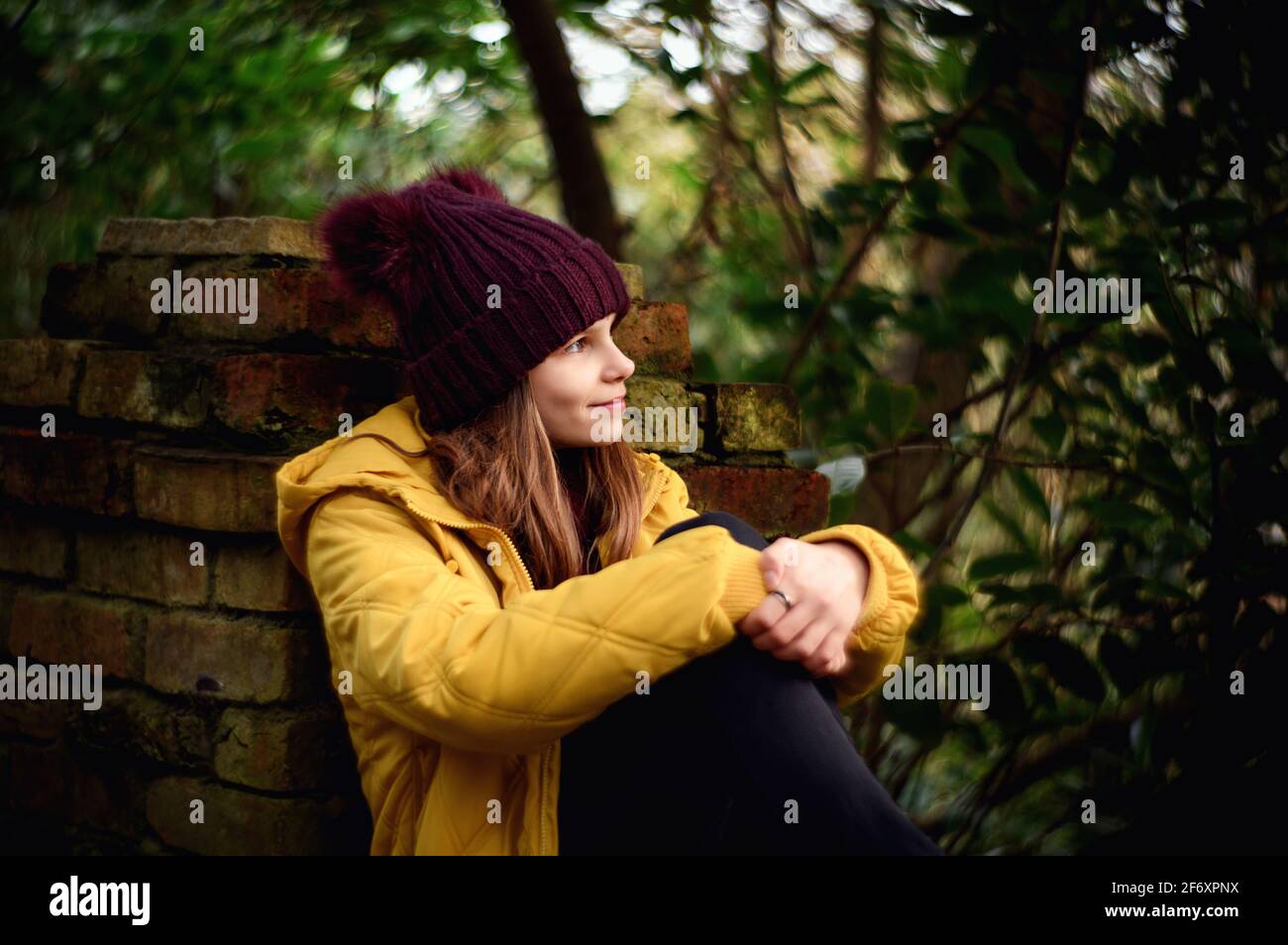 Lächelndes Mädchen, das im Herbst an einer Wand sitzt, Irland Stockfoto