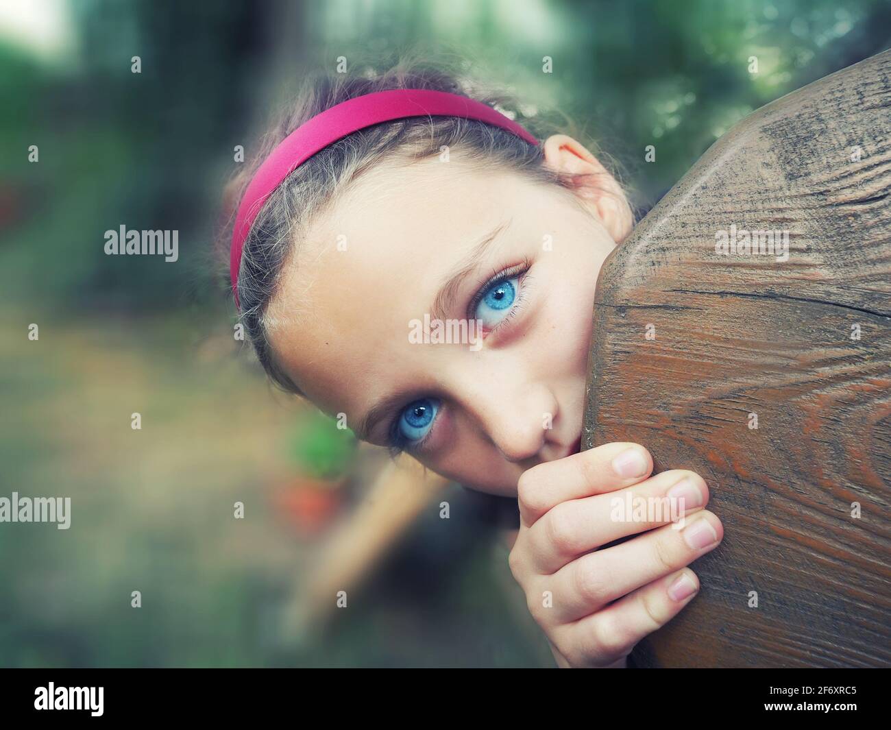 Schönes Mädchen, das hinter einer Holzbank in einem Garten, Polen, herausguckt Stockfoto