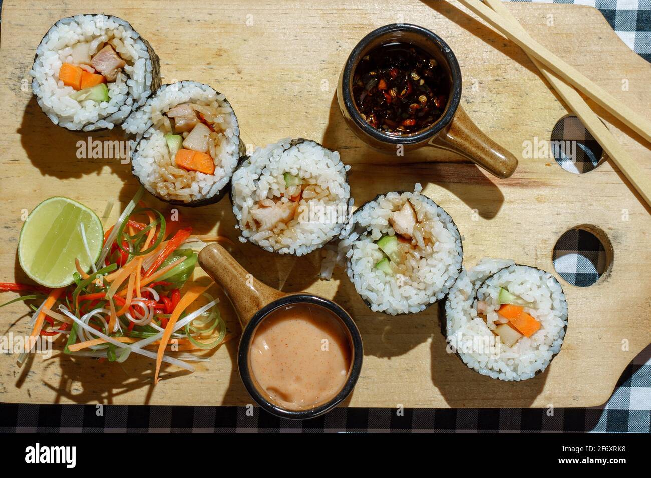 Blick von oben auf Sushi-Maki-Rollen auf einem Schneidebrett Mit Chili und würziger Sauce Stockfoto