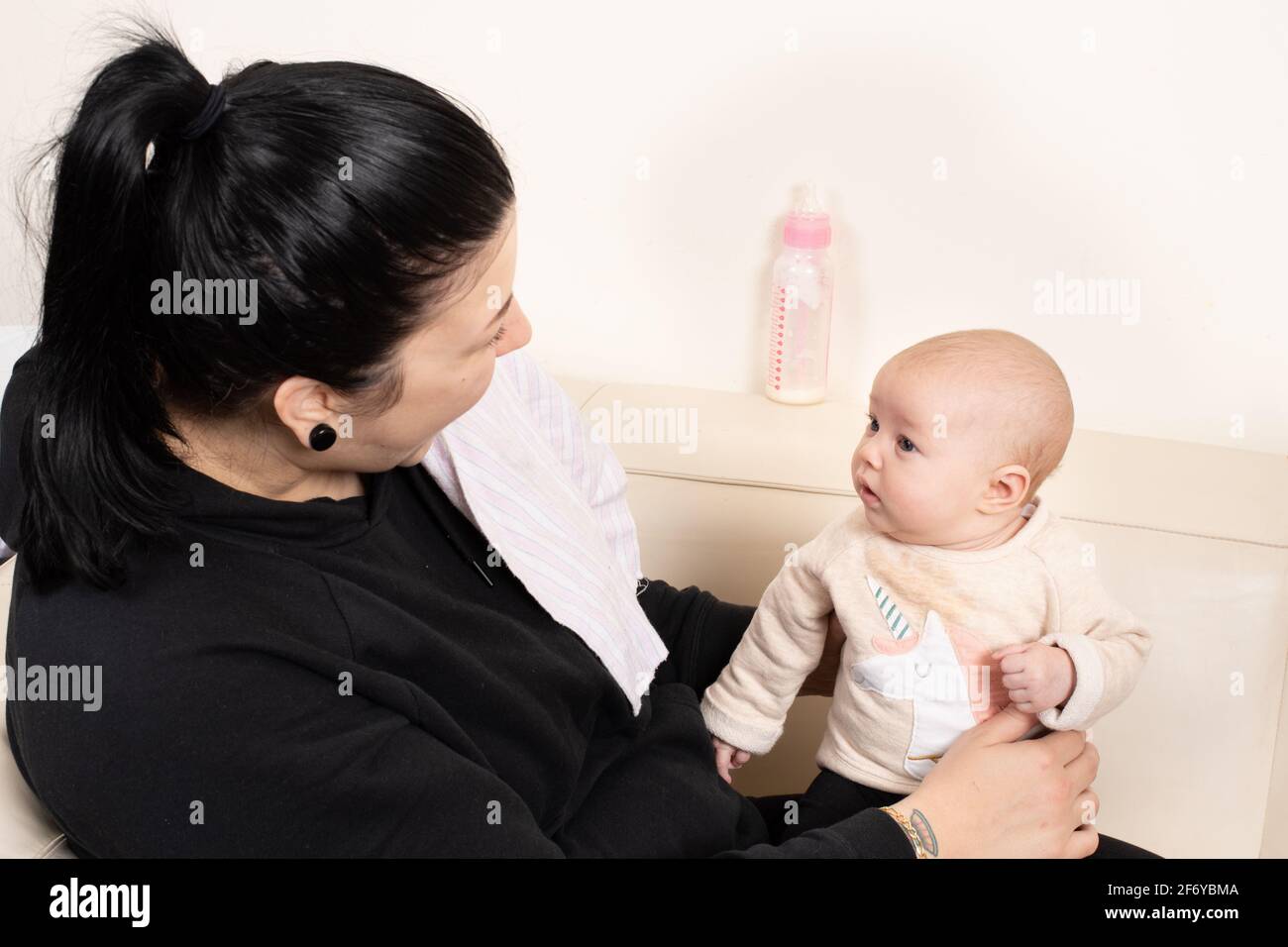 Zwei Monate altes Mädchen, das von der Mutter gehalten wird und sie aufmerksam anschaut, während sie spricht und lächelt Stockfoto
