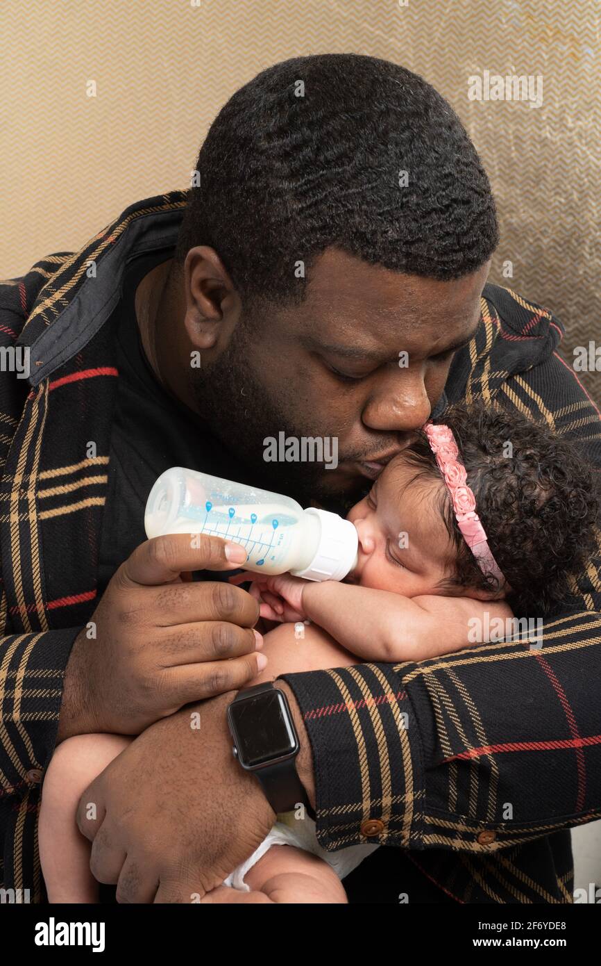 Neugeborenes Mädchen 3 Wochen alt, gefüttert Flasche von Vater, der ihren Kopf küsst, während sie trinkt Stockfoto