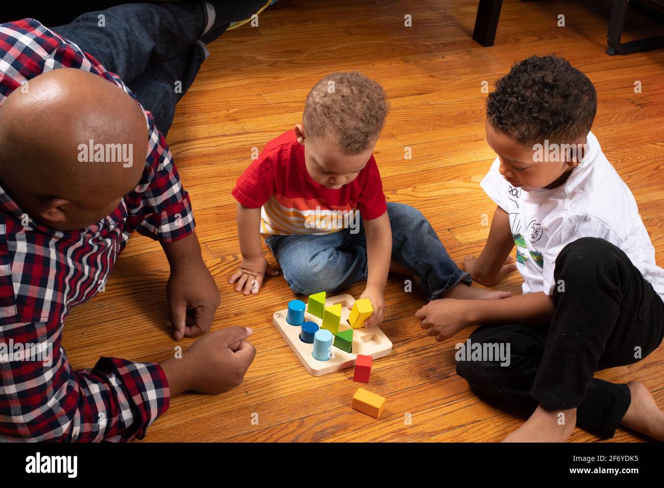 Brüder im Alter von 2 und 6 Jahren, die mit geometrischem Formsortierer spielen, während der Vater auf sie schaut Stockfoto