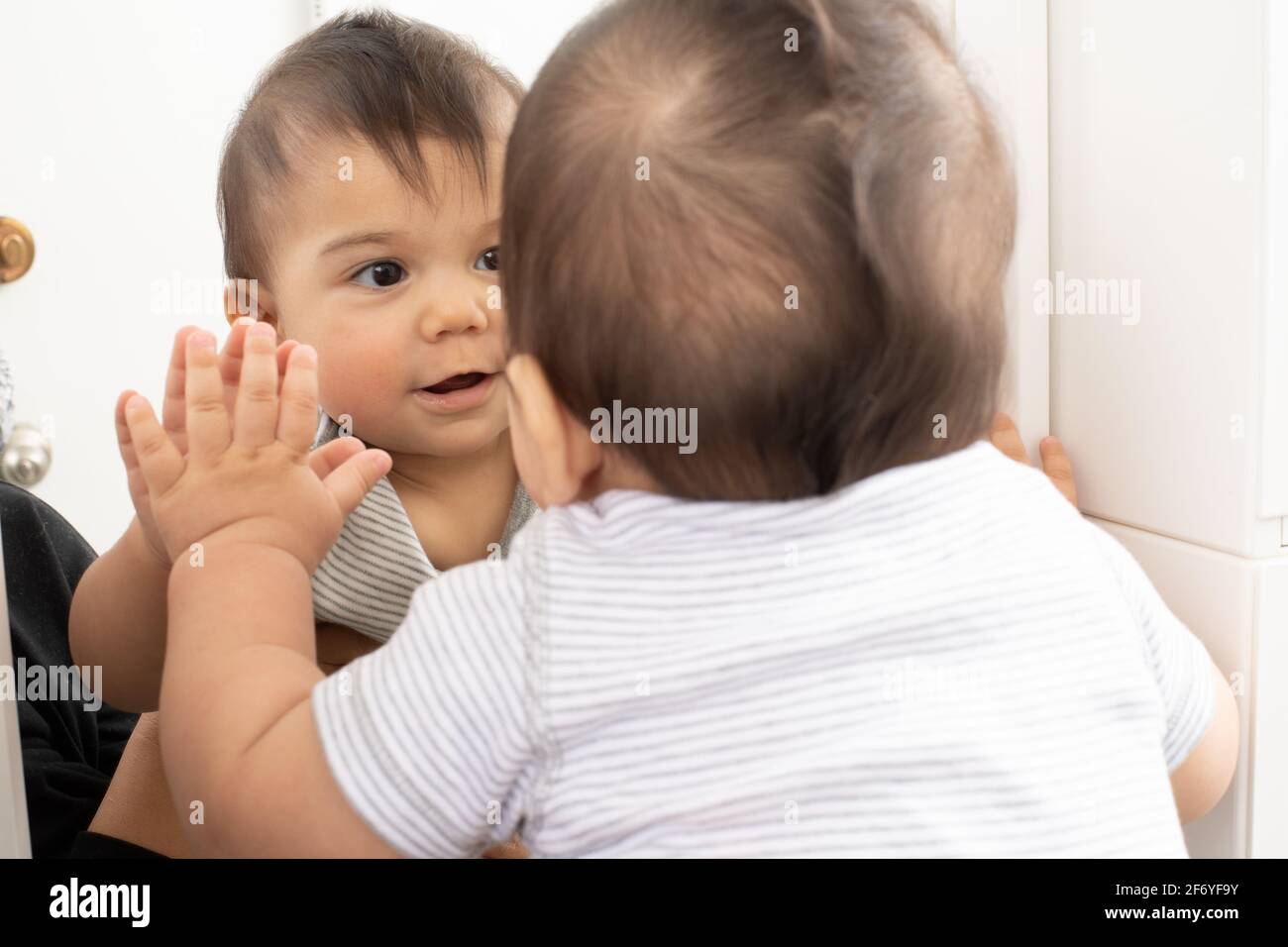 8 Monate alter Junge Nahaufnahme betrachtet seine Spiegelung im Spiegel und weiß nicht, dass es seine eigene Spiegelung ist Stockfoto