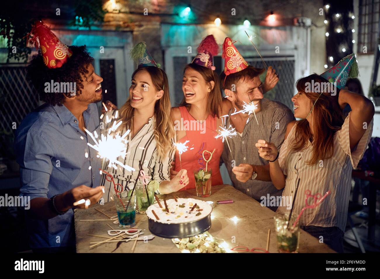 Eine Gruppe von Freunden, die an einem schönen Sommerabend mit Sprinklern auf der Open-Air-Geburtstagsfeier spielten. Gute Zeit der Freundschaft Stockfoto