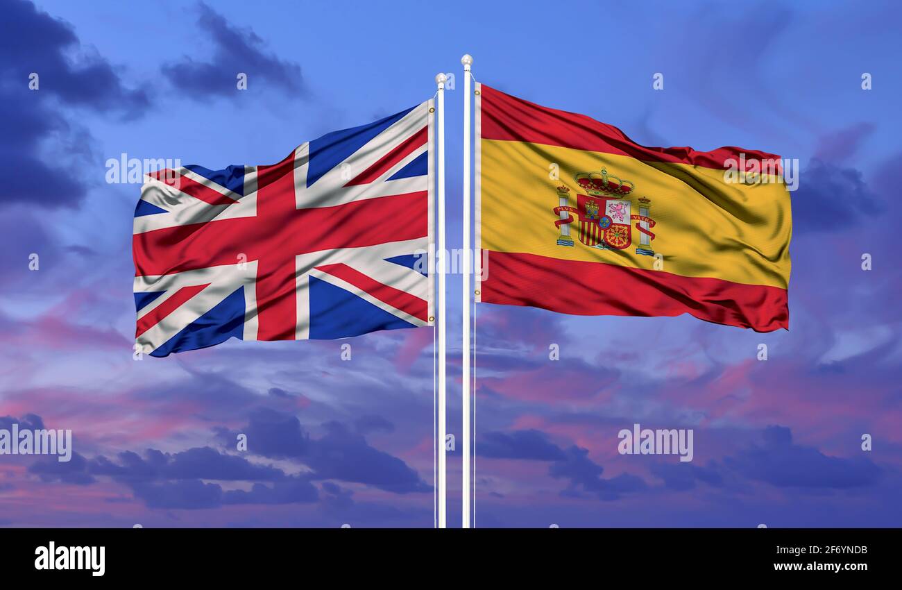 Großbritannien und Spanien Flagge winken im Wind gegen weiß wolkig blauen Himmel zusammen. Diplomatie Konzept, internationale Beziehungen Stockfoto