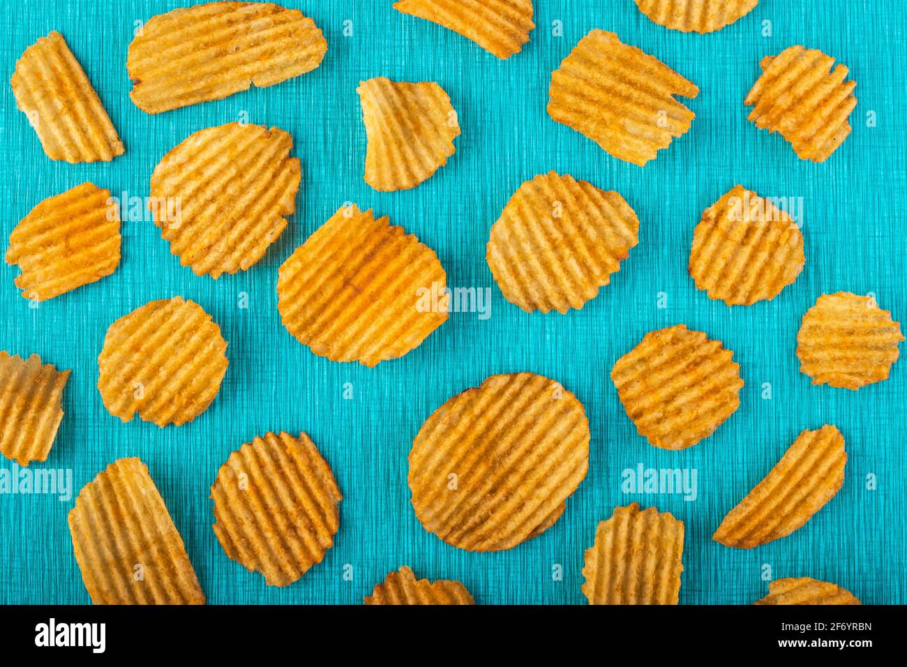 Kartoffelchips, gerillte Goldchips, knusprige Snacks aus Wellpappe auf türkisfarbenem Hintergrund, farbiges Muster. Ungesunde Fast Food. Textur mit gesalzenen Scheiben. Hig Stockfoto