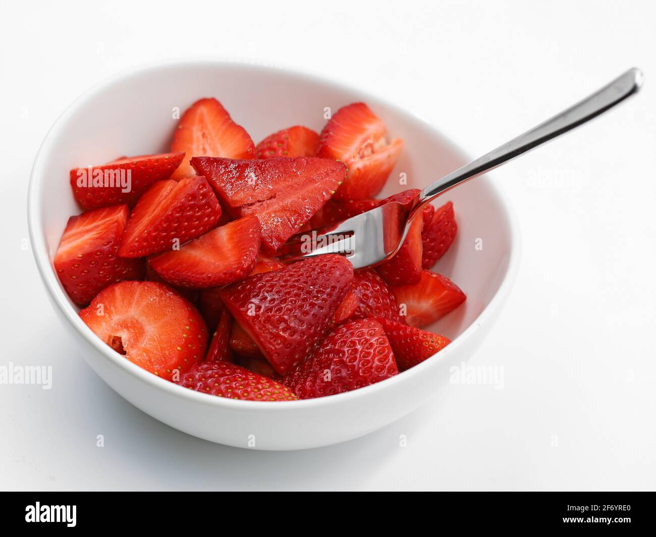 Weiße Schüssel voll von geschnittenen Erdbeeren mit Gabel auf weiß Hintergrund Stockfoto