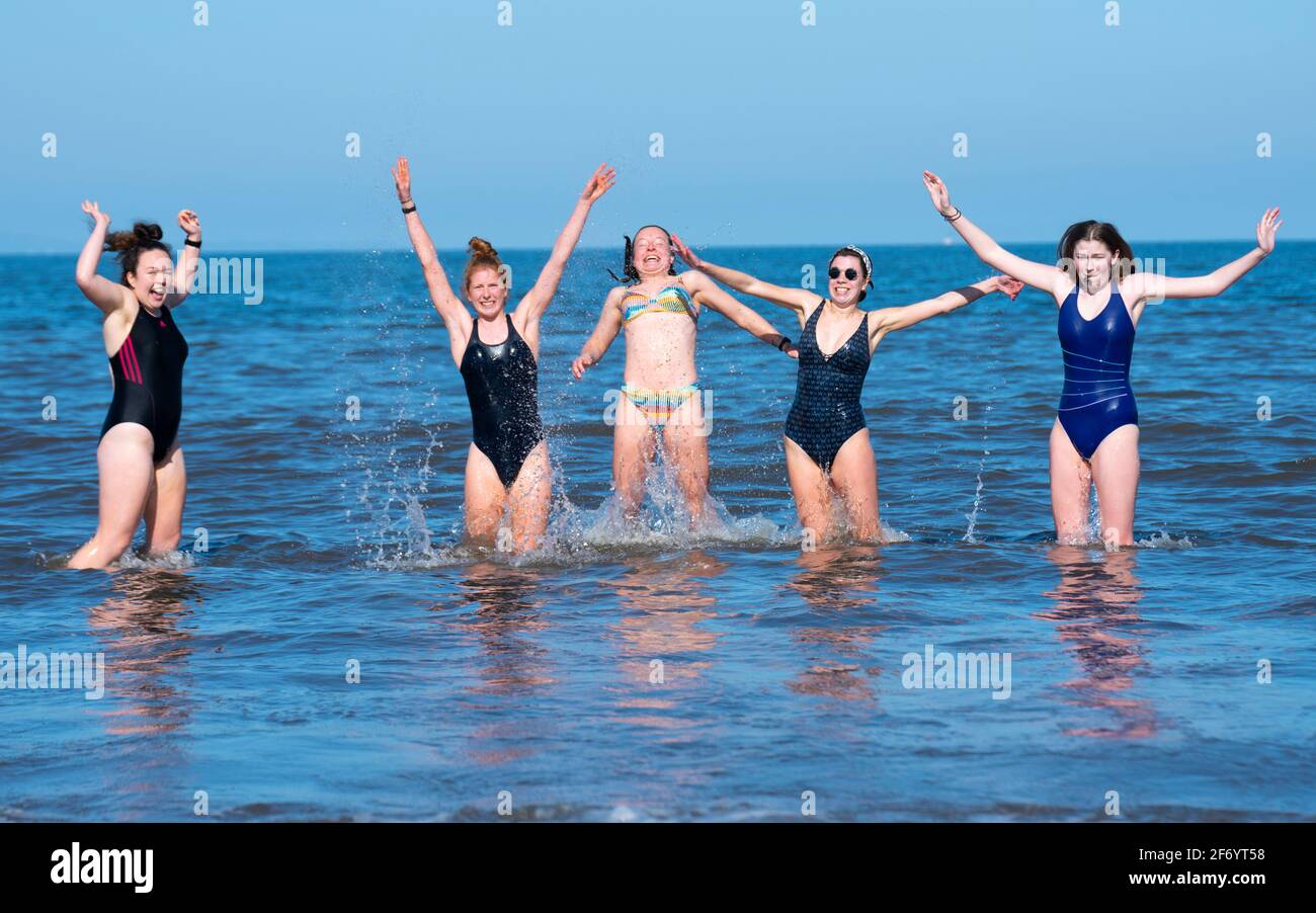 Portobello, Schottland, Großbritannien. 3. April 2021. Am Osterwochenende strömen Massen an den Strand und die Promenade von Portobello, um das Beste aus den neu entspannten Reisebeschränkungen von Covid-19 und der warmen Sonne mit ununterbrochenem blauen Himmel zu machen. PIC; fünf junge Frauen aus Edinburgh genießen ein Bad im Meer. Iain Masterton/Alamy Live News Stockfoto
