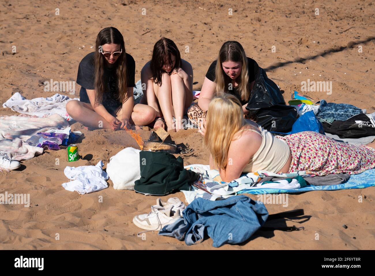 Portobello, Schottland, Großbritannien. 3. April 2021. Am Osterwochenende strömen Massen an den Strand und die Promenade von Portobello, um das Beste aus den neu entspannten Reisebeschränkungen von Covid-19 und der warmen Sonne mit ununterbrochenem blauen Himmel zu machen. PIC; vier junge Frauen, die sich an einem Holzfeuer entspannen. Iain Masterton/Alamy Live News Stockfoto