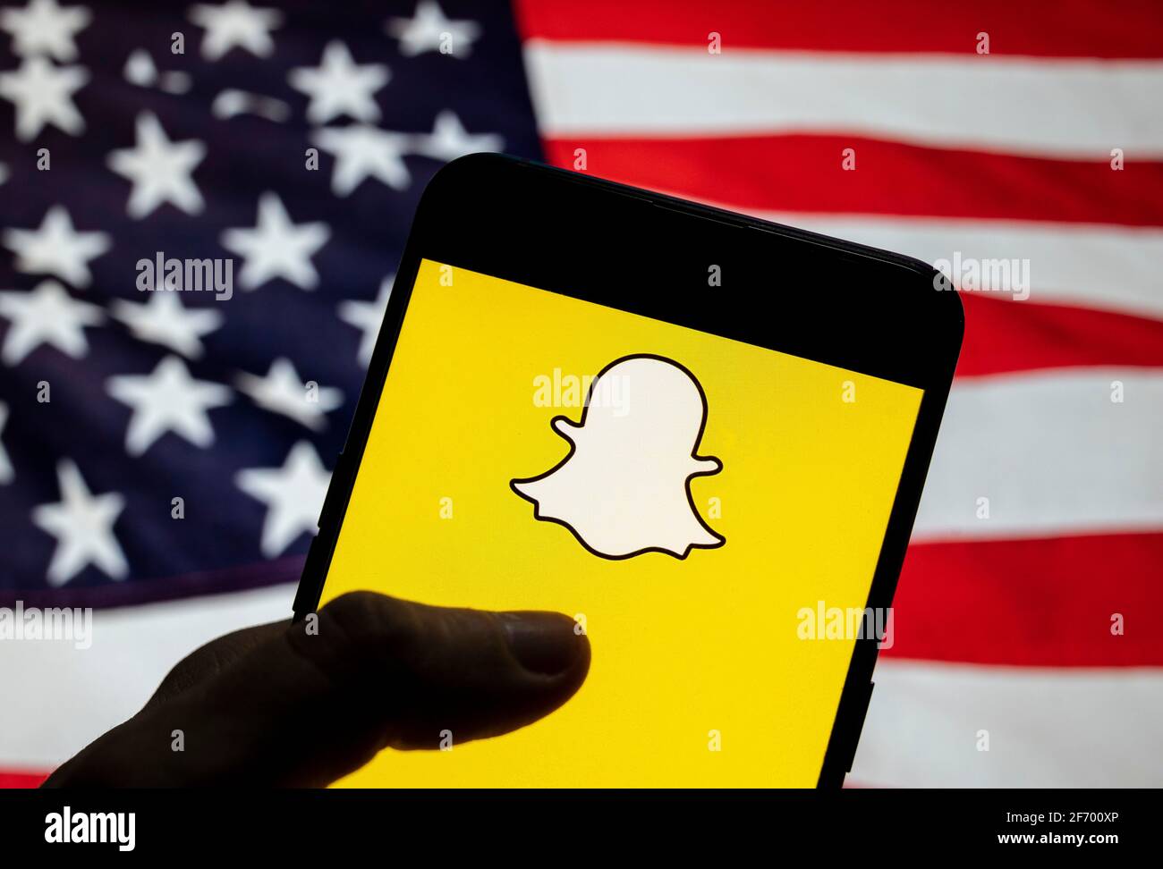 In dieser Abbildung wird das Snapchat-Logo für Multimedia-Nachrichten auf einem Smartphone mit einer Flagge der Vereinigten Staaten im Hintergrund angezeigt. Stockfoto
