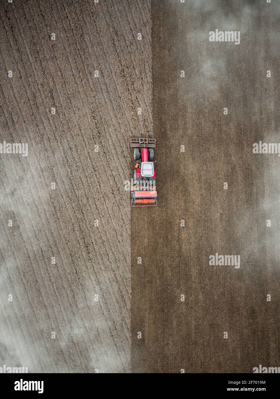 Roter Traktor pflügt Feld Luftaufnahme von oben durch Wolken. Drohnen Anbau Maschine Ausrüstung arbeiten Pflügen Land Stockfoto