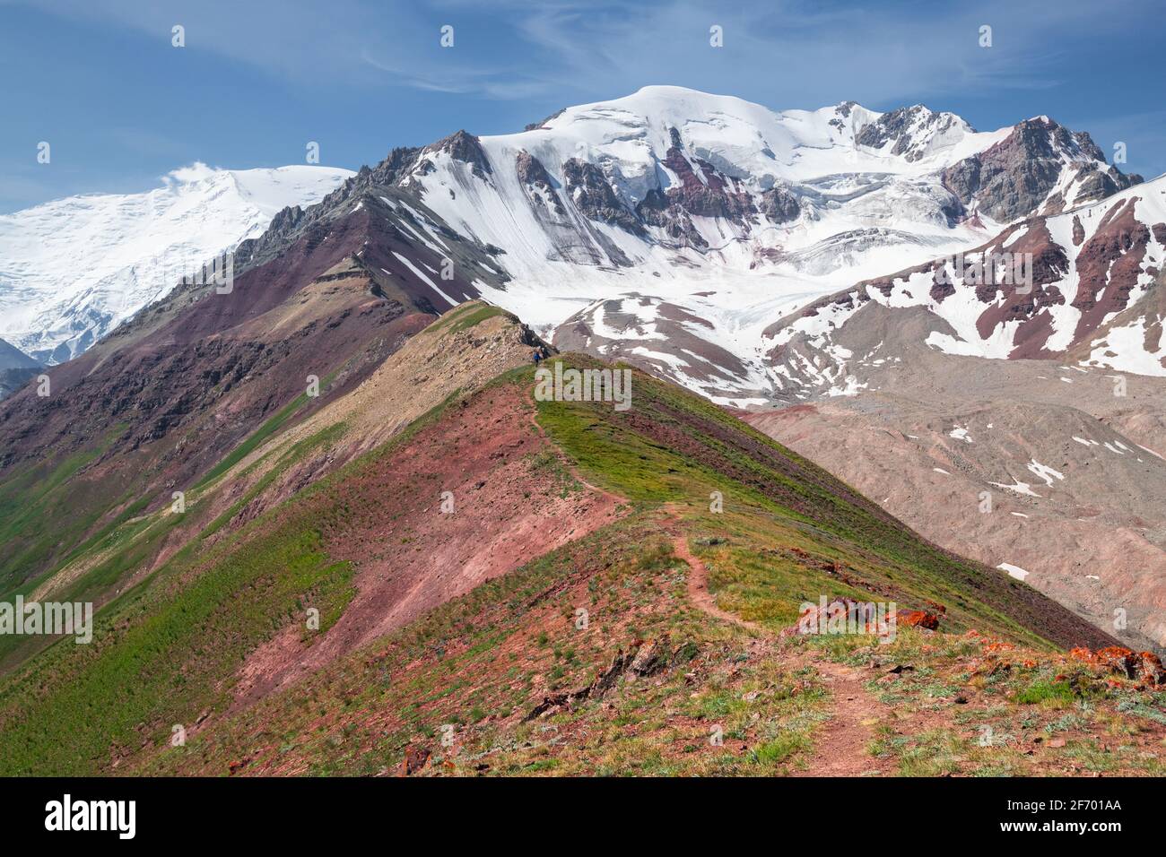 Bergweg auf dem steilen Grat an einem sonnigen Tag Am Fuße des schneebedeckten Lenin-Gipfels im Pamir-Gebirge An der Grenze zwischen Kirgisistan und Tadschikistan Stockfoto