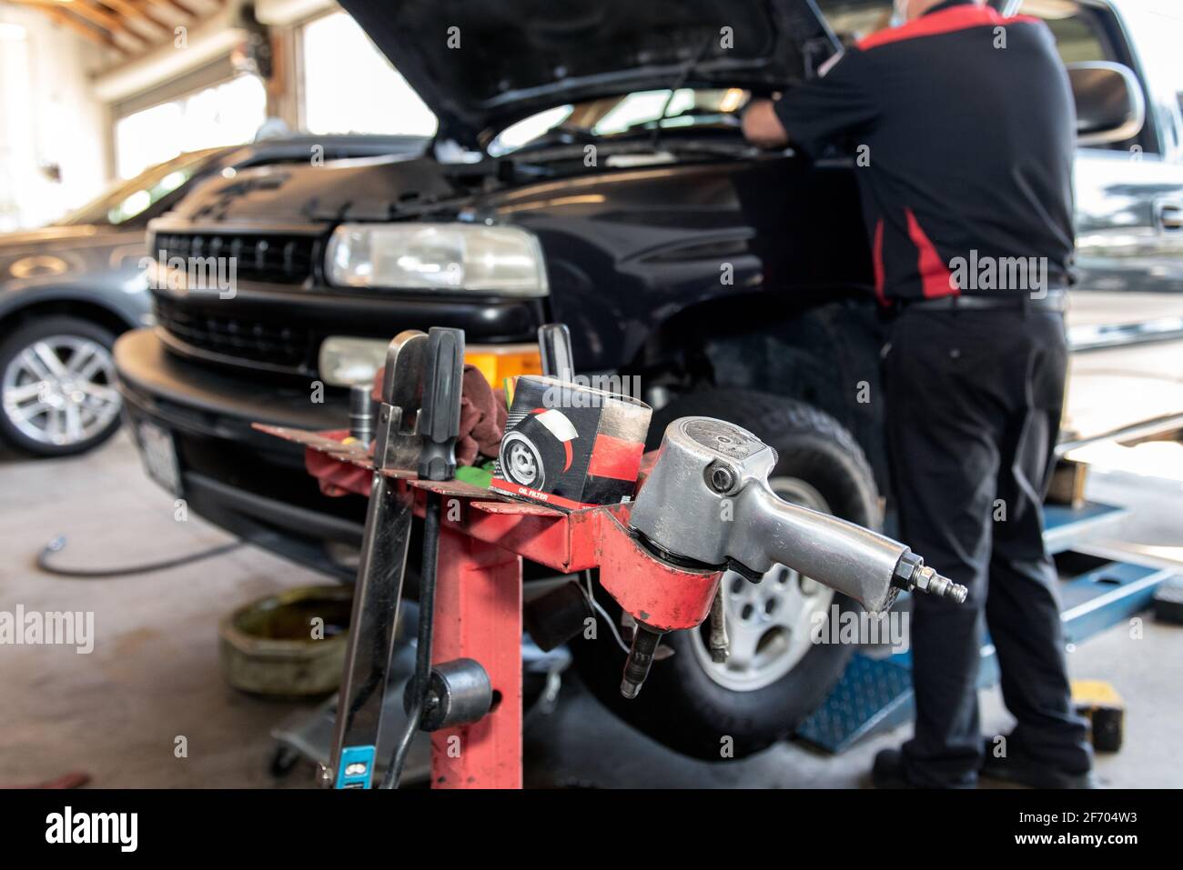 Schlagschrauber und Steckschlüssel sind für den Einsatz durch Mechaniker bereit, der während des Ölwechsels unter die Motorhaube des Fahrzeugs schaut. Stockfoto