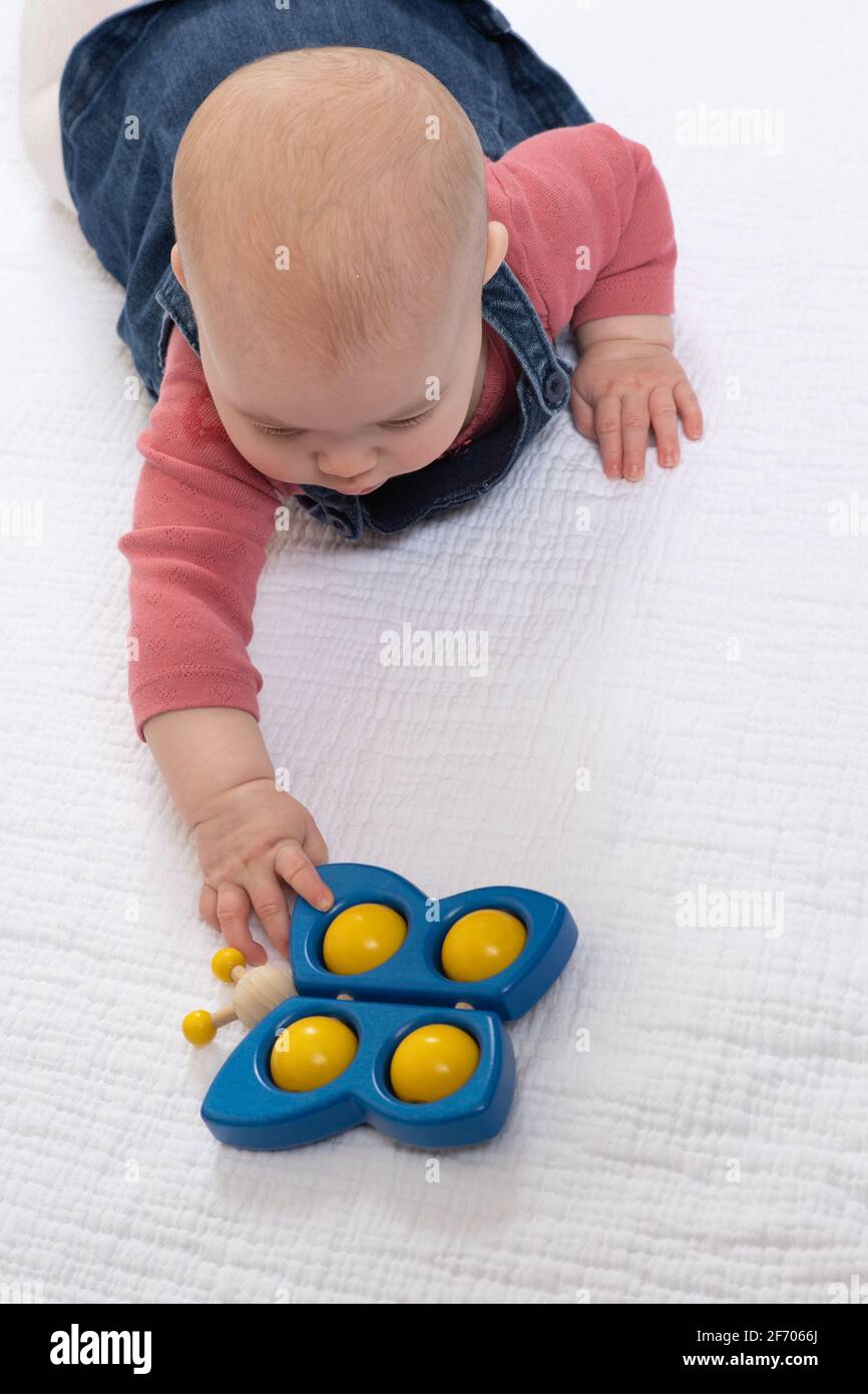 4 Monate altes Baby Mädchen, auf dem Bauch, nach Spielzeug greifen, bunte hölzerne Schmetterling Spielzeug Stockfoto