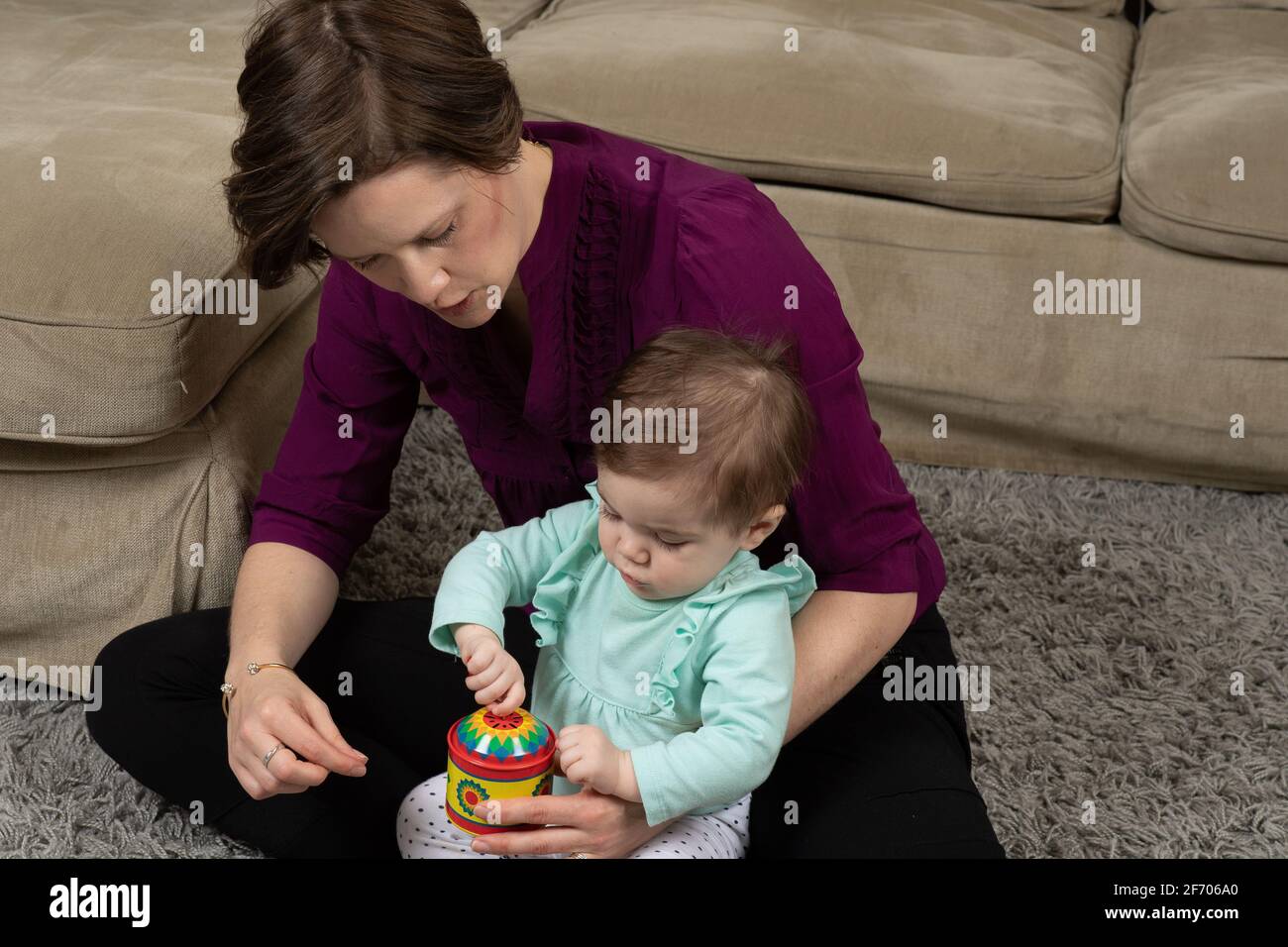 10 Monate altes Mädchen mit Mutter, das versucht, die Kurbel am Musikspielzeug zu drehen, nachdem es gezeigt wurde, wie es funktioniert Stockfoto