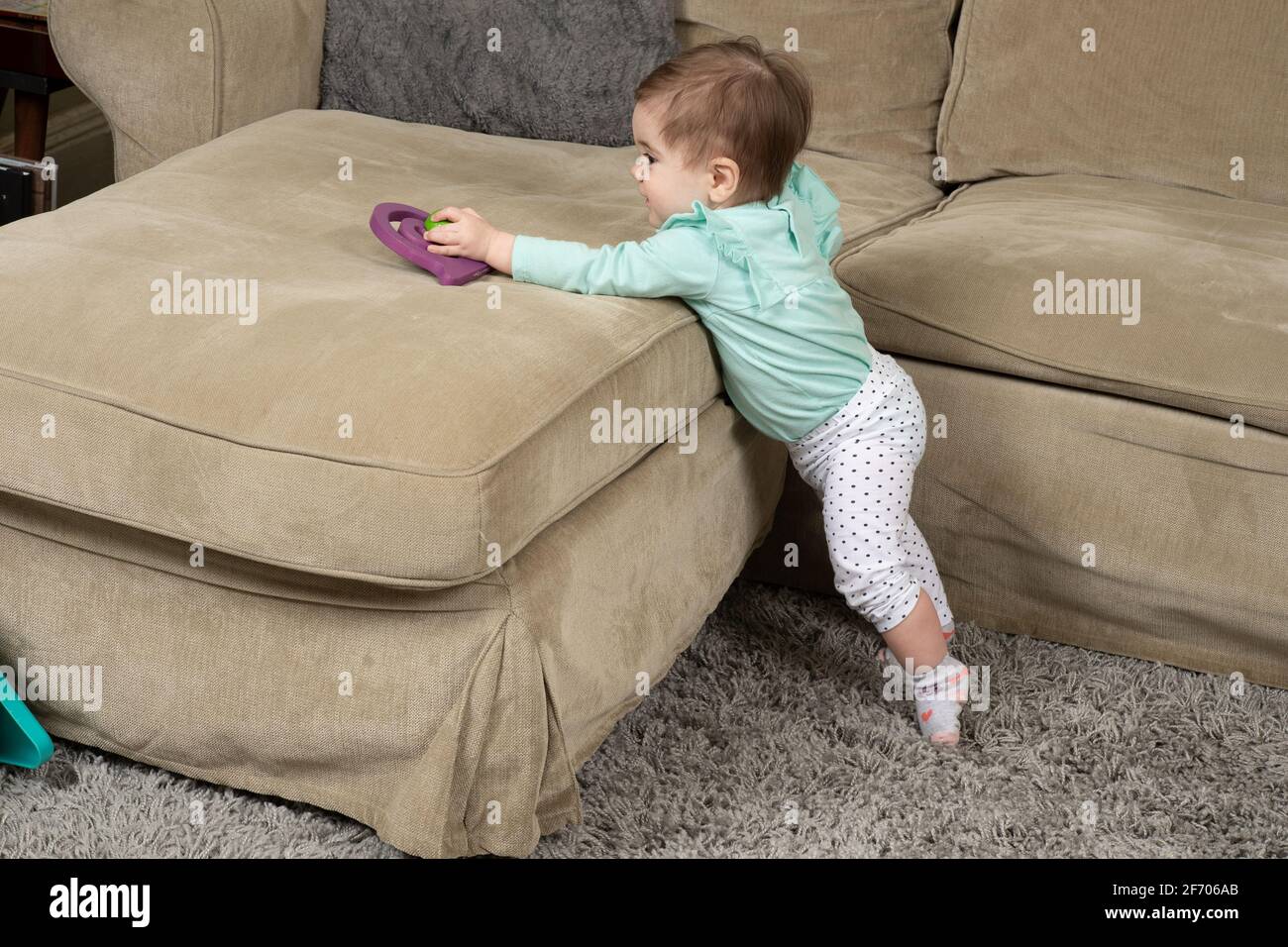 10 Monate altes Mädchen, das auf Zehenspitzen steht und nach Spielzeug greift Stockfoto
