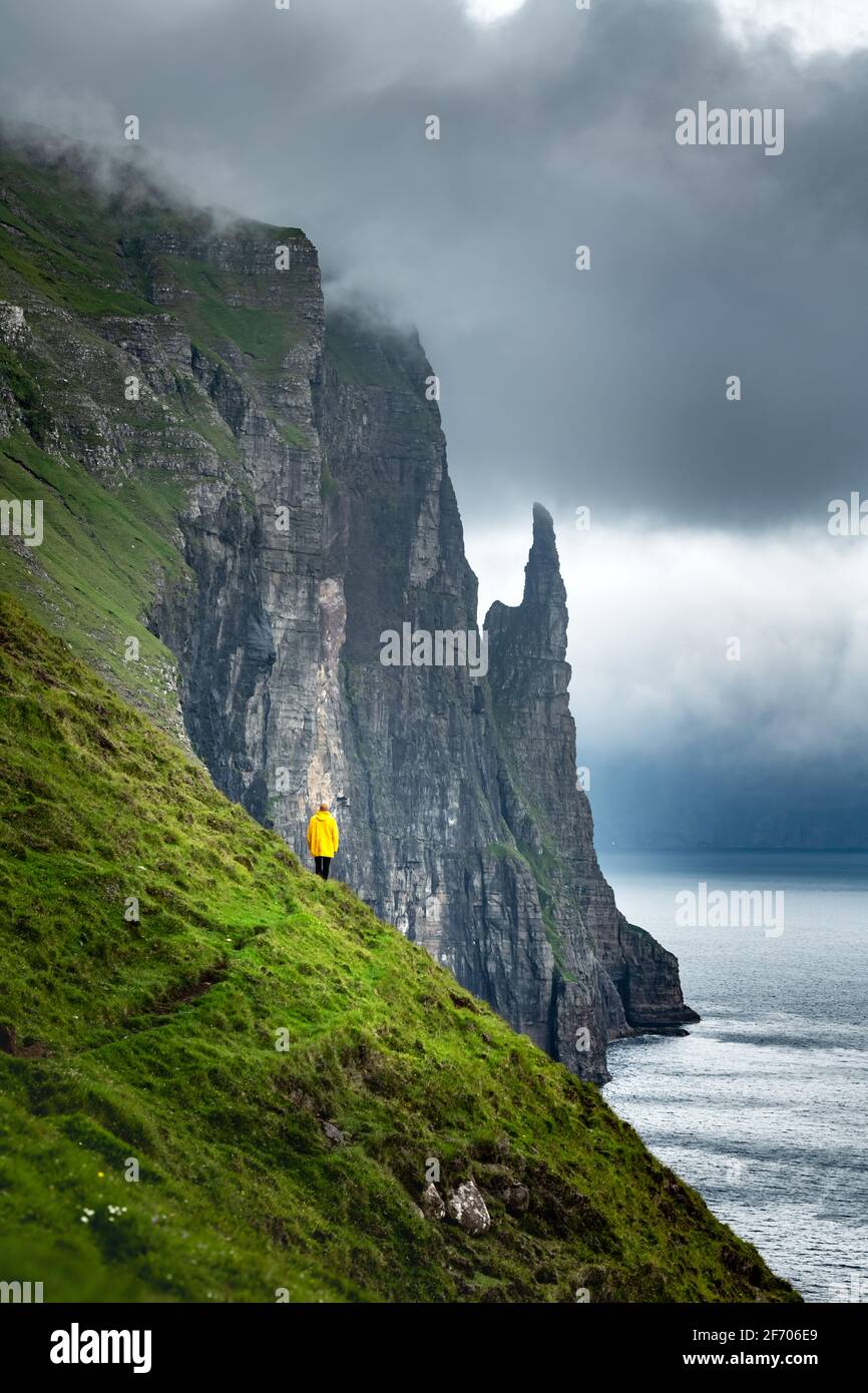 Touristen in der gelben Jacke sieht sich Hexen Finger Klippen von Trollkonufingur Aussichtspunkt. Vagar Island, Färöer, Dänemark. Stockfoto