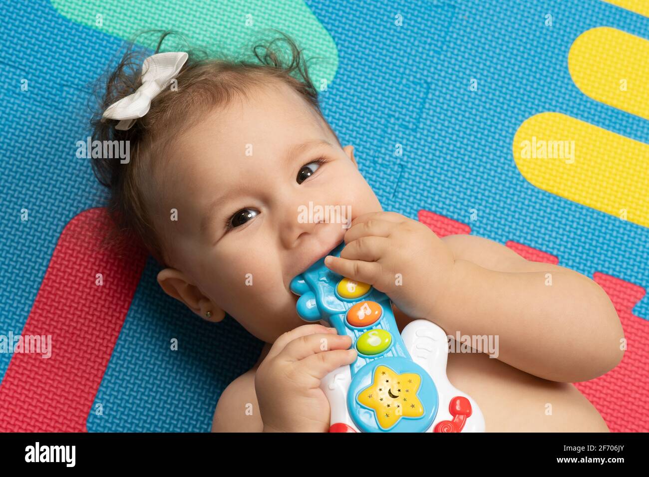 7 Monate altes Baby Mädchen Nahaufnahme auf dem Rücken mouthing Plastikspielzeug, Finger im Mund Stockfoto