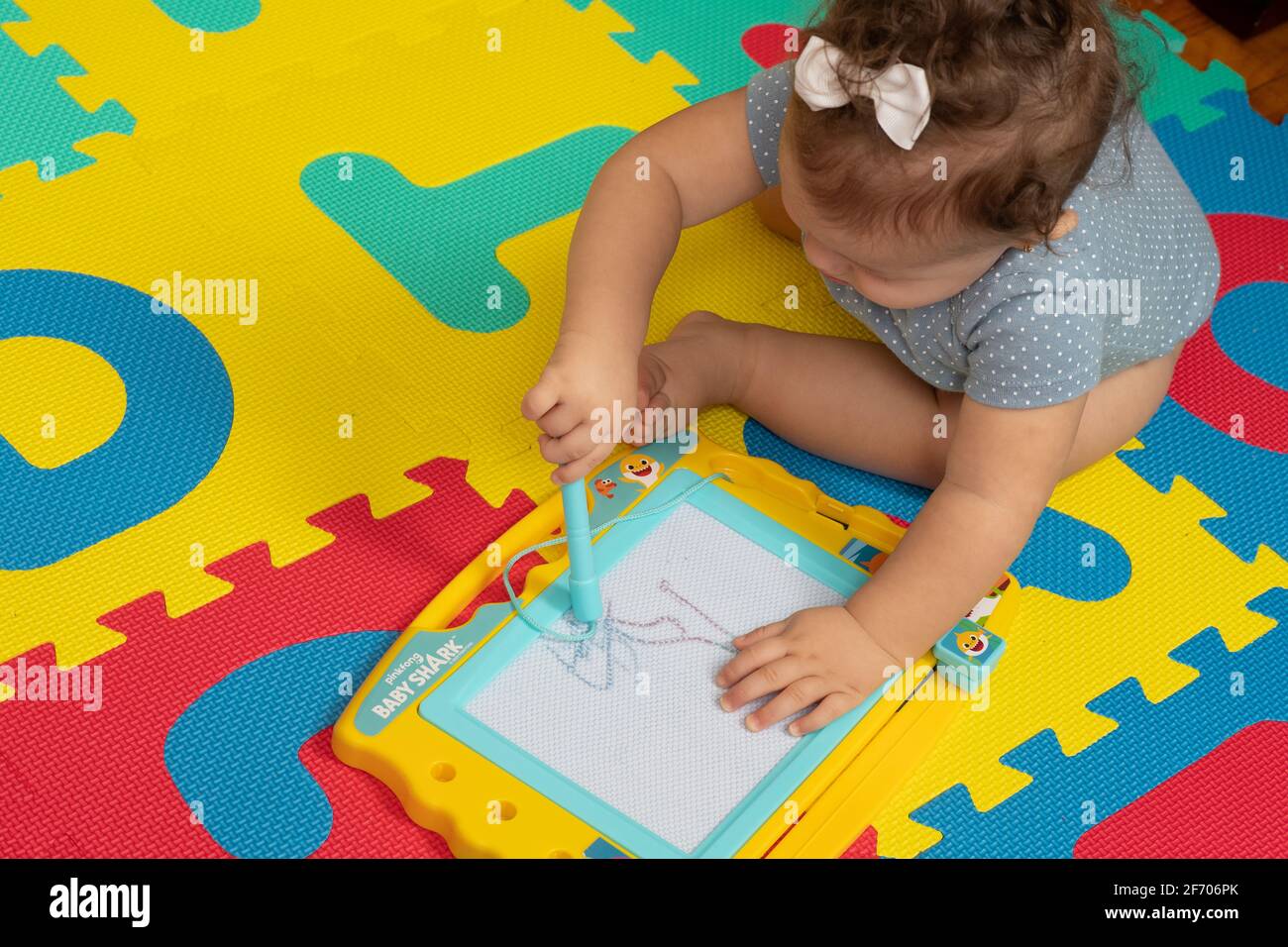 Das 7 Monate alte Mädchen sitzt und macht mit dem Zeichenstab auf einer Tablette, ähnlich einem Skizzen-Ätzchen, mit etwas als Instrument Stockfoto