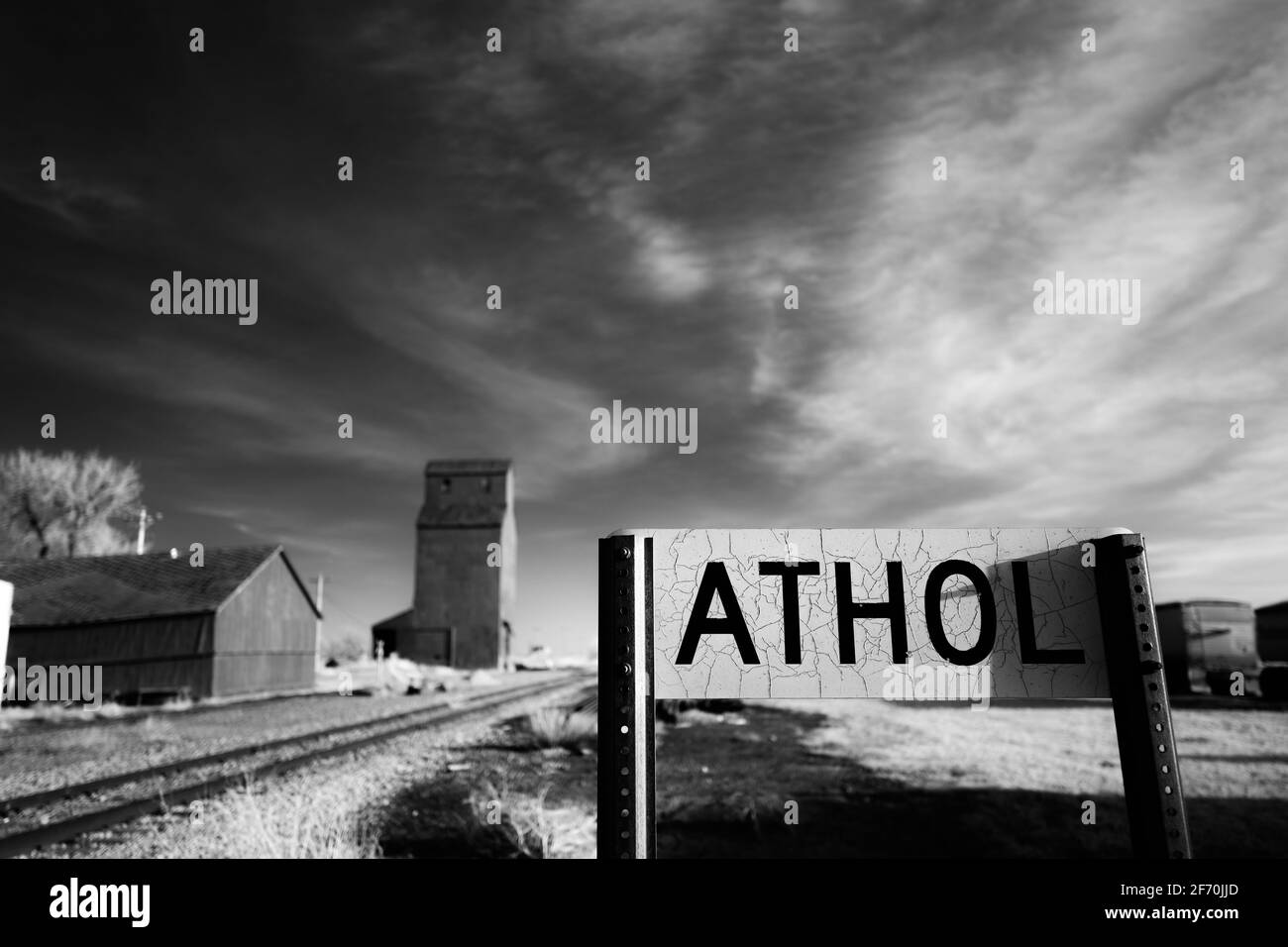 Das rissige Eisenbahnmarkierungszeichen für Athol, South Dakota, mit einigen landwirtschaftlichen Strukturen im Hintergrund des schwarz-weißen Infrarotbildes. Stockfoto