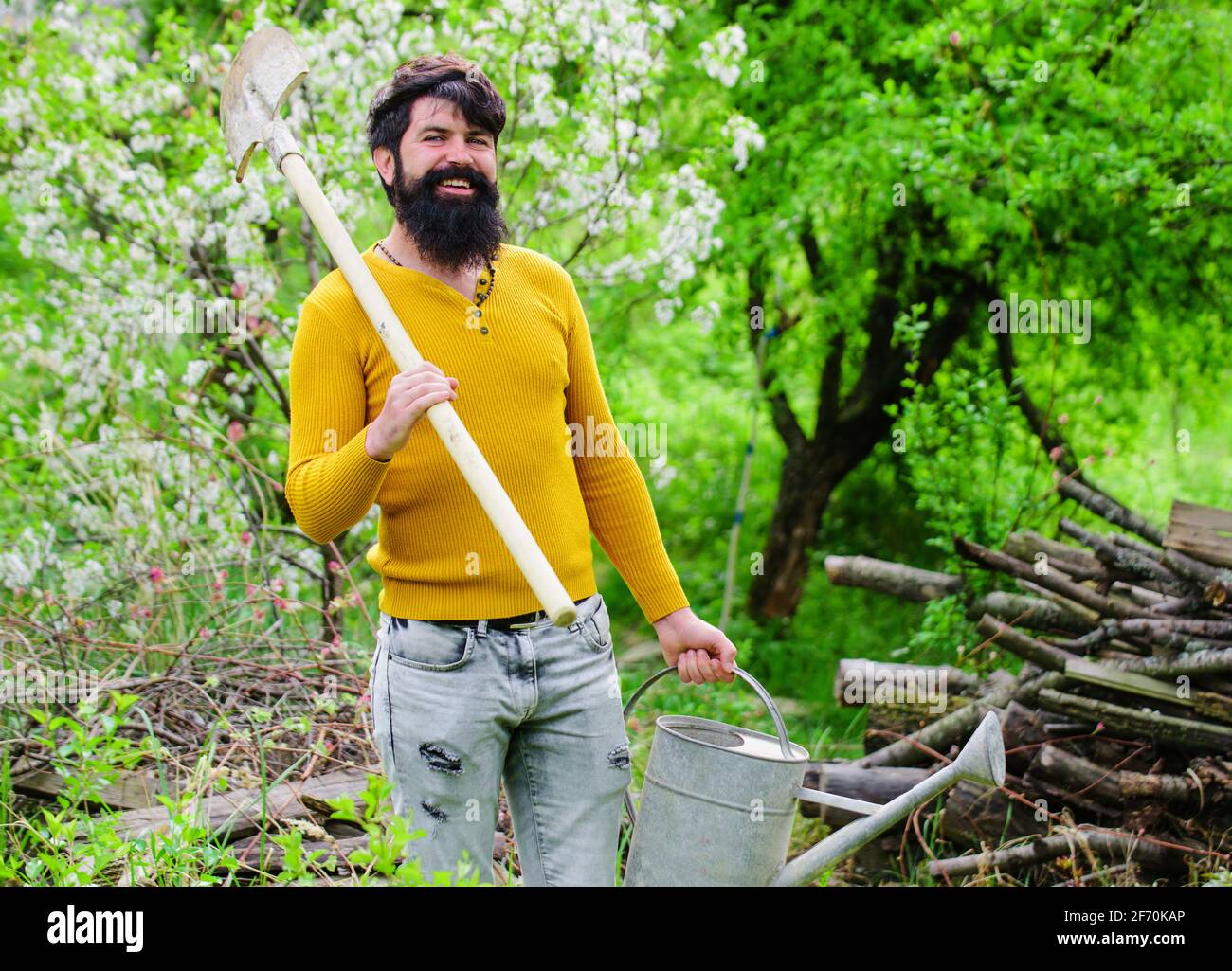 Bewässerung. Gartenarbeit. Lächelnder Gärtner mit Gießkanne und Spaten. Arbeiten im Garten. Bauernhof. Frühling Stockfoto