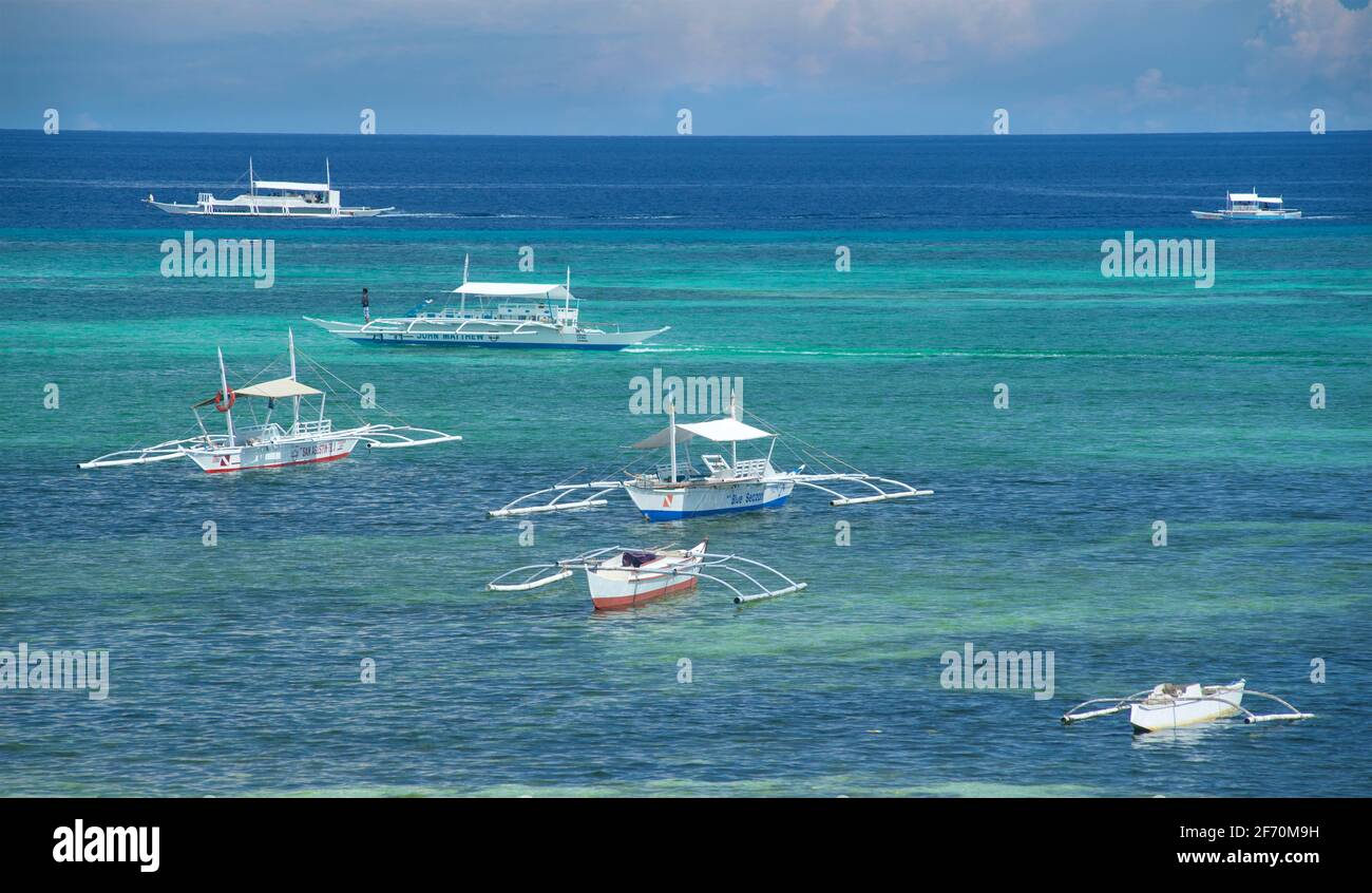 Eine Flotte von Auslegerkanus vor Doljo Beach, Panglao Island, Bohol, Philippinen, vor Anker. Türkisblaues und azurblaues tropisches Wasser. Stockfoto