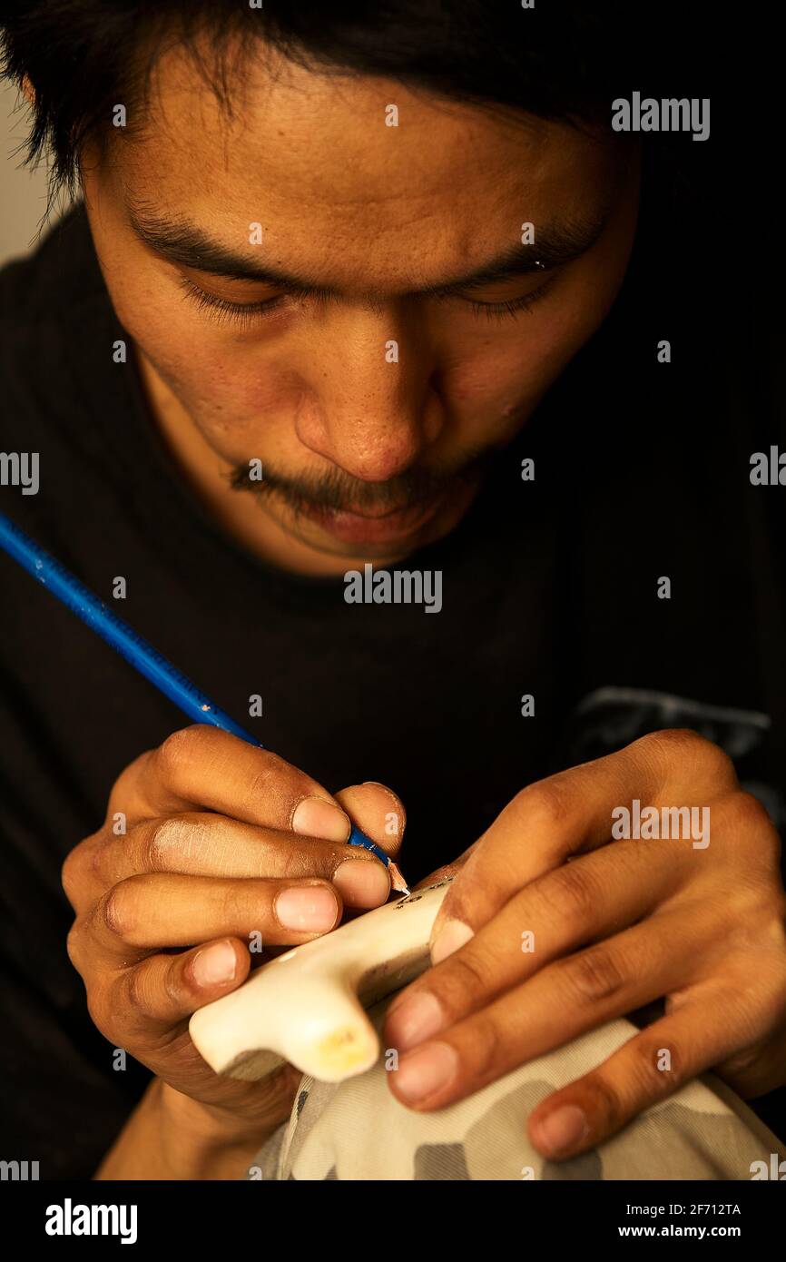 Nahaufnahme der Hände des Inuit-Künstlers, die an seinem Arbeitsplatz in Pond Inlet, Nunavut, zarte Linien in eine Knochenschnitzerei gravieren. Stockfoto
