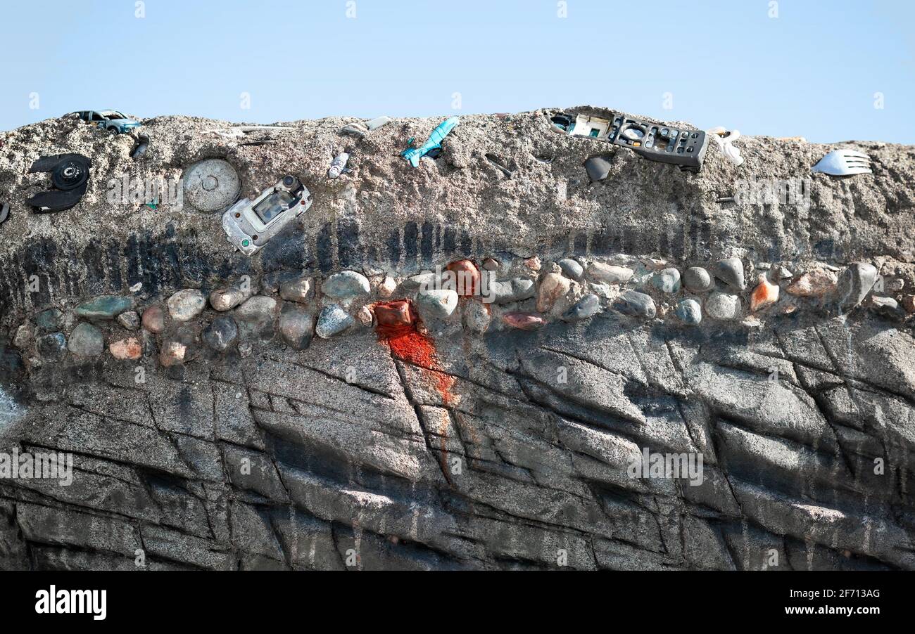Alttechnologiemüll teilweise im Boden eingebettet. Alte Telefone, Computerteile und Tonbandgeräte in Sedimentation und Gesteinsschichten. Stockfoto
