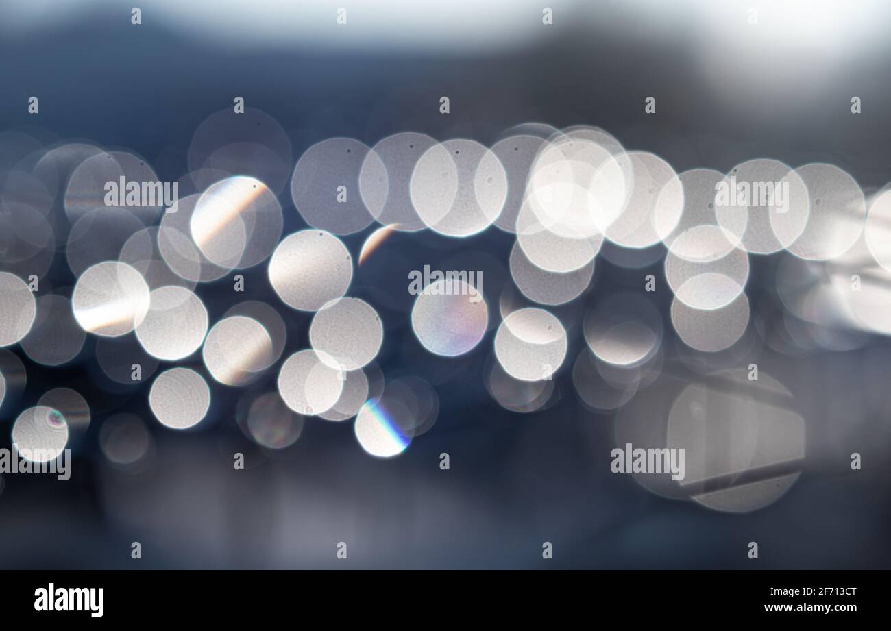 Bokeh Lichter von Wassertropfen auf Mesh draußen am frühen Morgen. Defokussierte und abstrakte weiße Äpfel, die in einer horizontalen Linie angeordnet sind. Stockfoto
