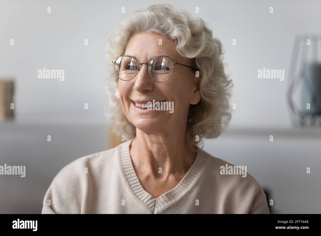 Eine fröhliche, nachdenkliche ältere Dame, die eine Brille trägt und auf das Fenster schaut Stockfoto