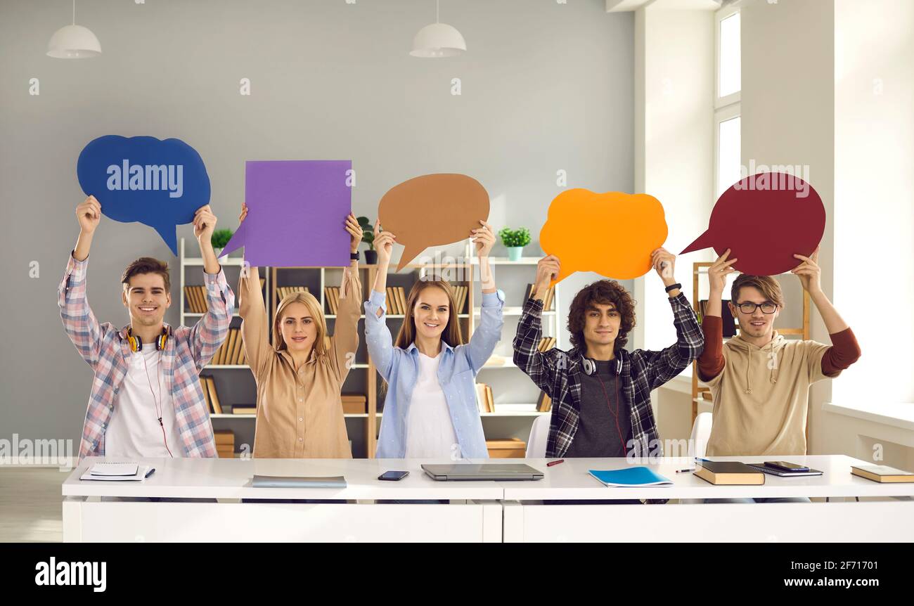 Glückliche Schüler oder Studenten sitzen am Schreibtisch und halten Leere Sprechblasen Stockfoto Glückliche Schüler oder Studenten sitzen am Schreibtisch und halten Leere Sprechblasen Stockfoto