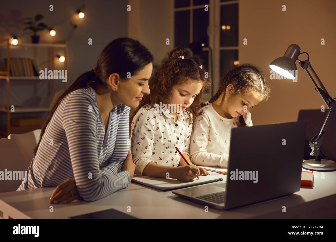 Die liebevolle Mutter sieht ihren Zwillingstöchtern beim Zeichnen zu, während sie sich Online-Zeichenunterricht auf einem Laptop ansieht. Stockfoto