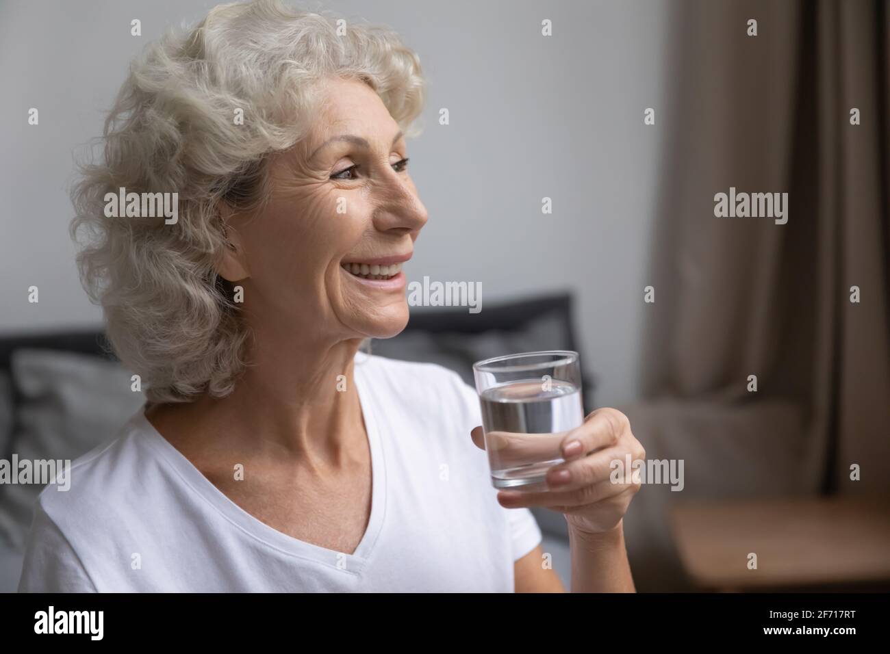 Fröhliche, nachdenkliche ältere Dame, die frisches, reines sauberes Wasser trinkt Stockfoto