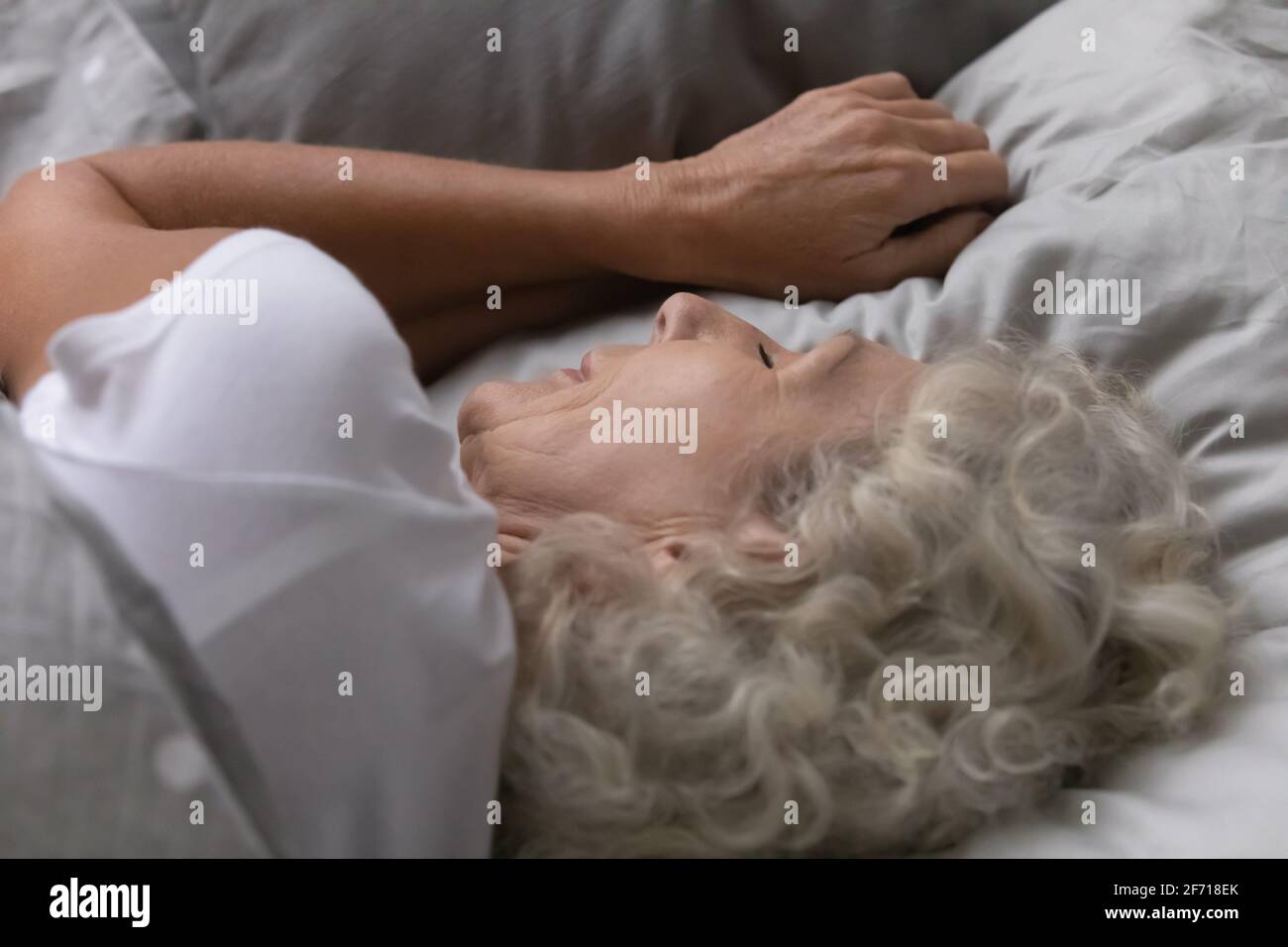 Friedliche, einsame ältere Dame, die sich in Leinenbettwäsche ausruhte Stockfoto