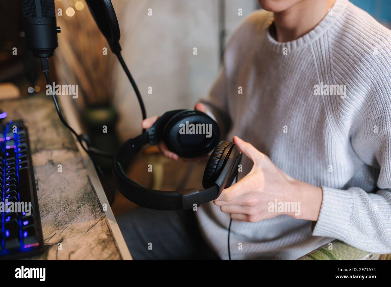Nahaufnahme eines Mannes mit Kopfhörern während der Arbeit mit Musik zu Hause. Hintergrund von Mikrophon und pc mit Tastatur. Neonlicht Stockfoto