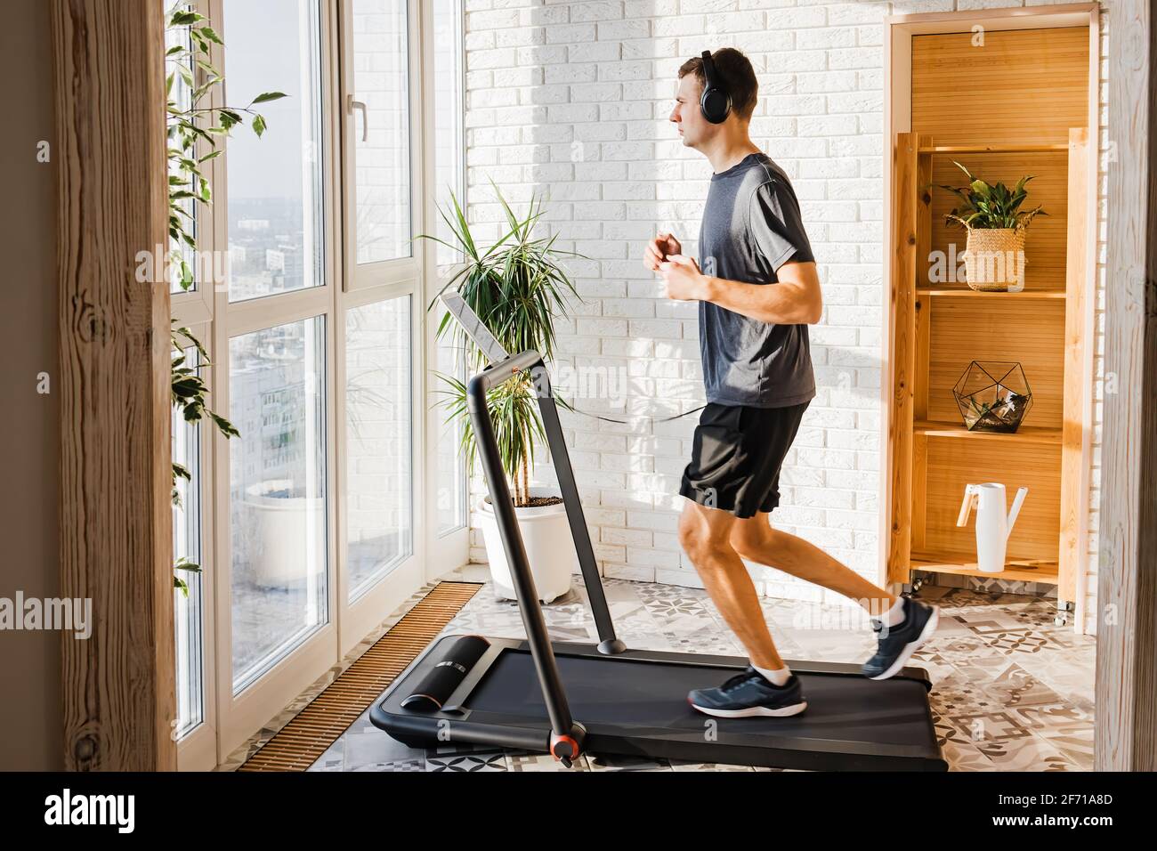 Der junge Mann joggt auf dem modernen kompakten Laufband bei ihm Zu Hause Stockfoto
