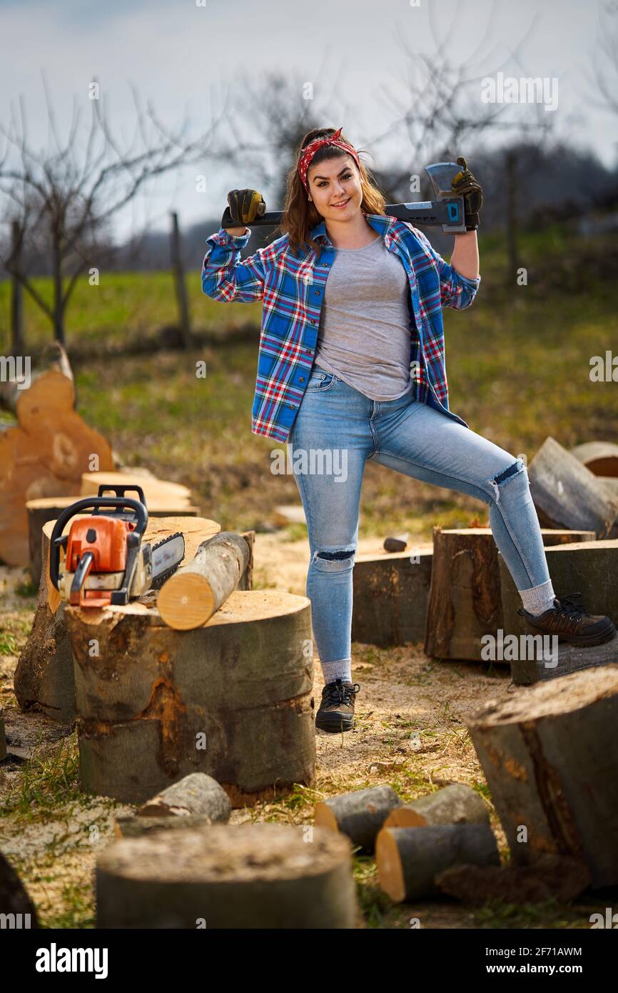 Starke Holzfällerin mit ihrer Axt und ihrer Kettensäge Riesige abgesägte Holzstämme Stockfoto