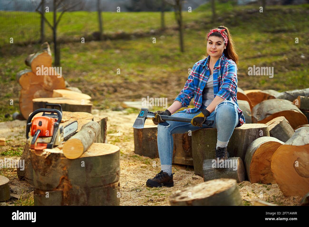 Starke Holzfällerin mit ihrer Axt und ihrer Kettensäge Riesige abgesägte Holzstämme Stockfoto
